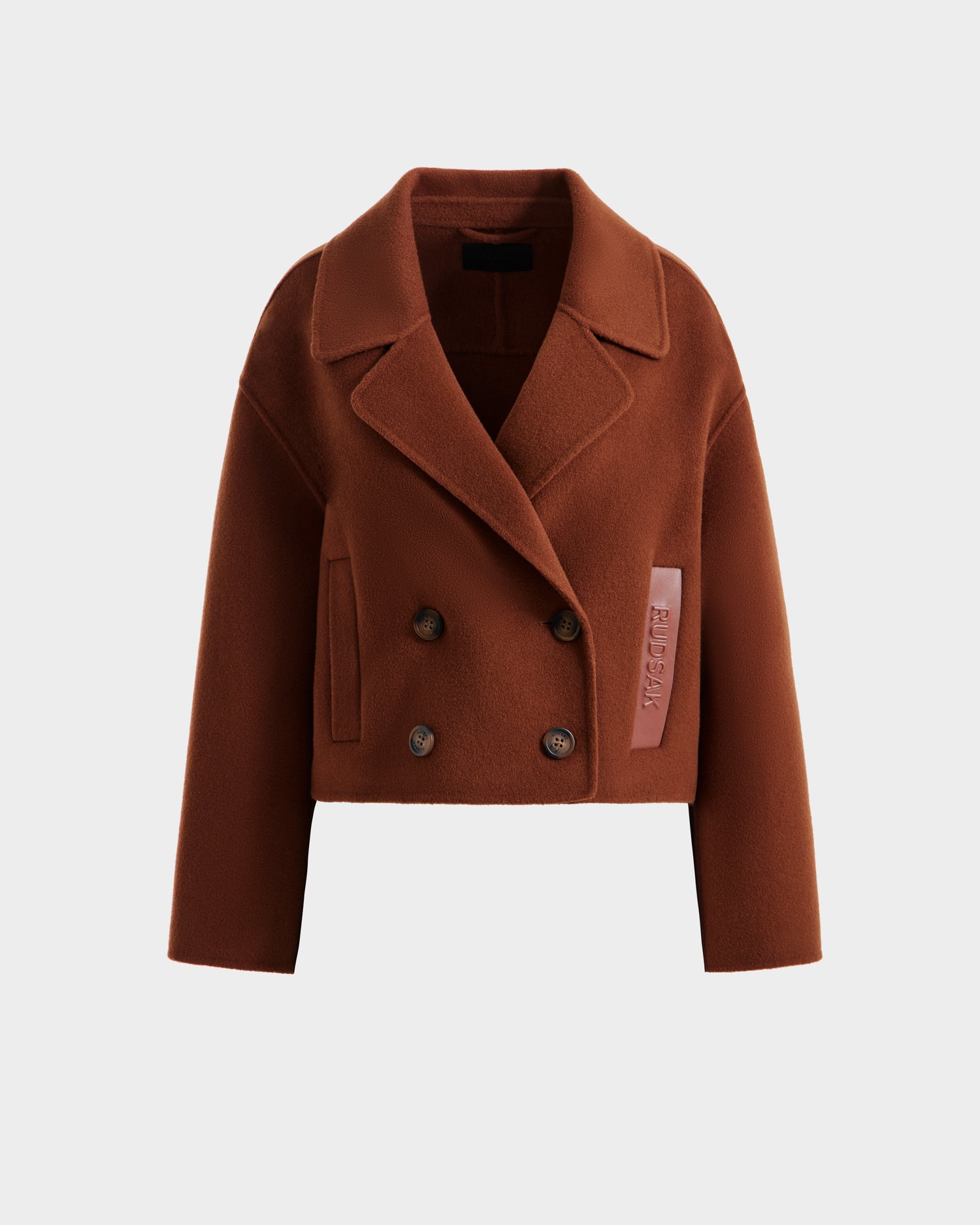 The Rudsak MARTINEZ - 8125580 Rust is a cropped, double-breasted women’s brown wool-blend coat with wide lapels, four front buttons, and a light pink fabric tag on one side, shown against a plain white background.