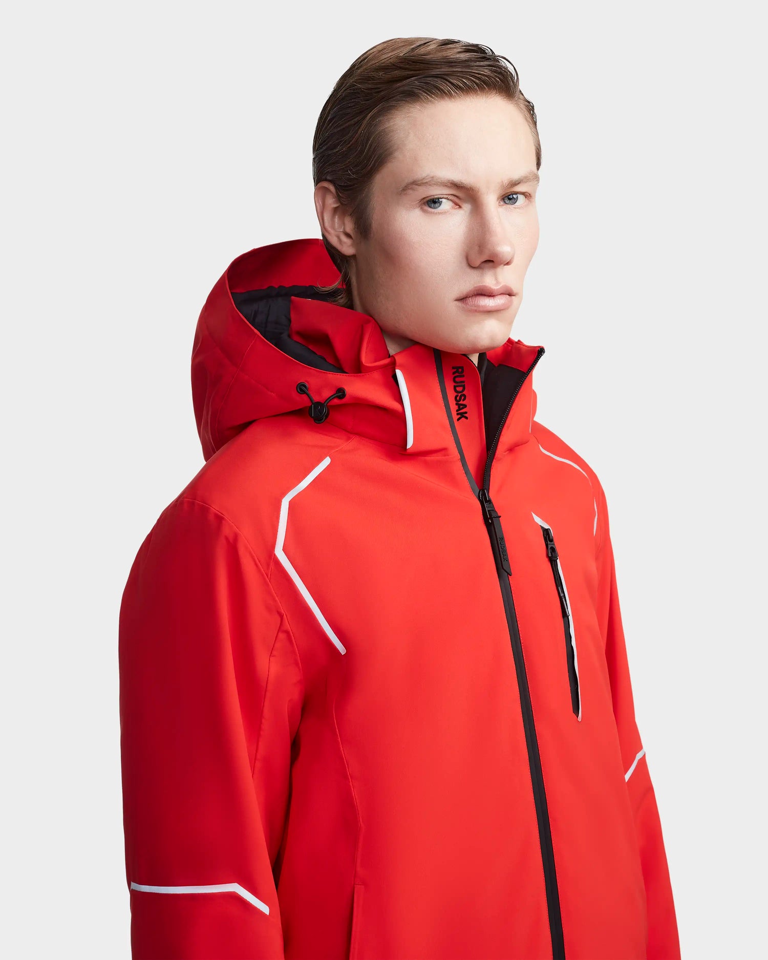 A young person with short, slicked-back hair wears the Rudsak EDMONTON - 6123520 Orange jacket, featuring bold black and white details, standing against a plain light gray background.