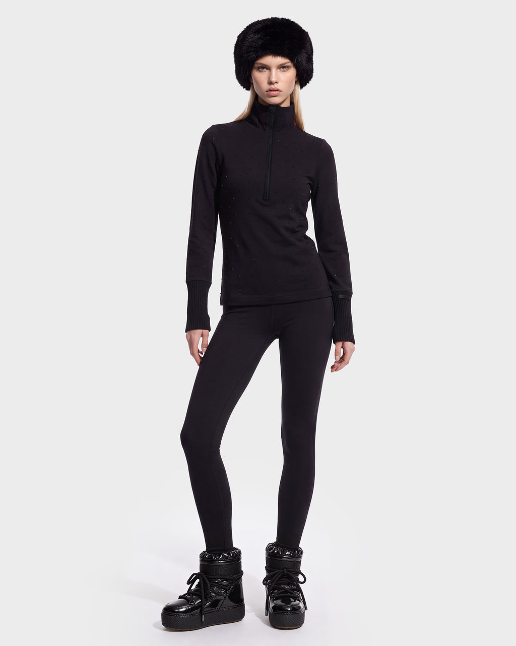 A model wears the NEVA - 8526524 Black fitted long-sleeve top in a stretch nylon blend, black leggings, black winter boots, and a black faux fur hat.
