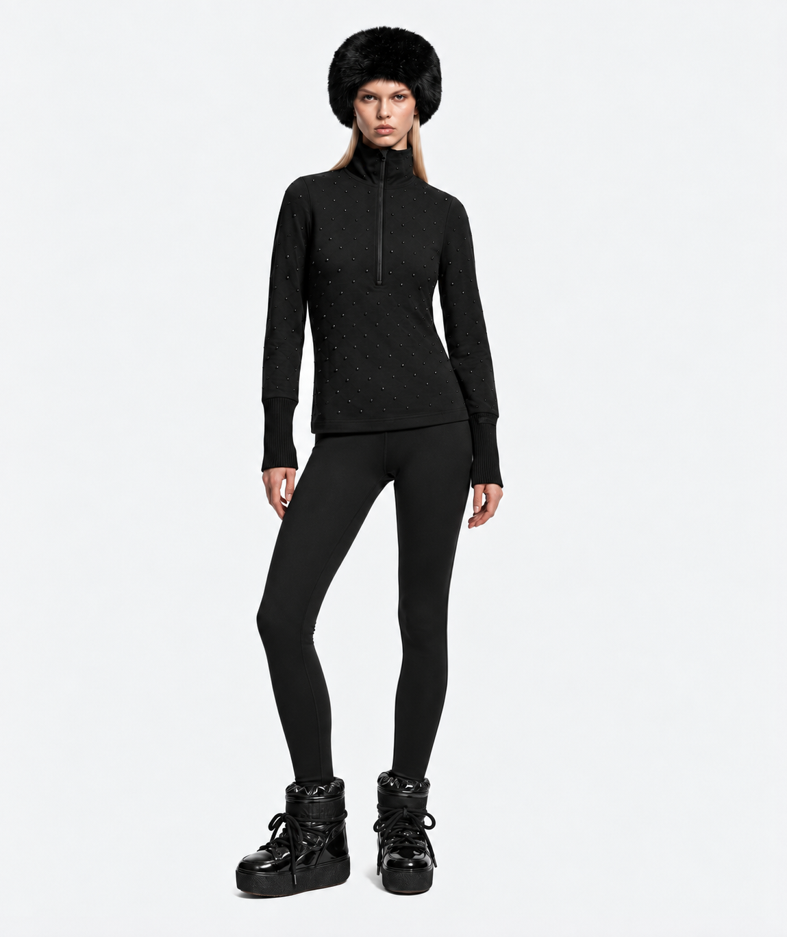 A woman wearing a faux fur hat, a black Rudsak NEVA - 8526524 Black après-ski top with stud detailing, black leggings, and black platform boots.