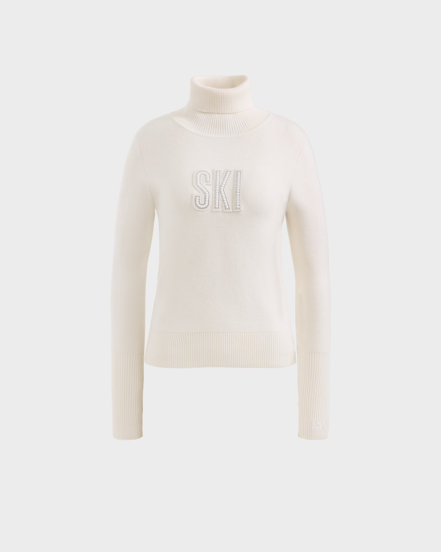 The NOVIE - 8525659 Vanilla by Rudsak is a cream knit women’s turtleneck sweater with ribbed cuffs and hem, featuring large textured SKI lettering—an ideal après-ski pullover for winter outings.