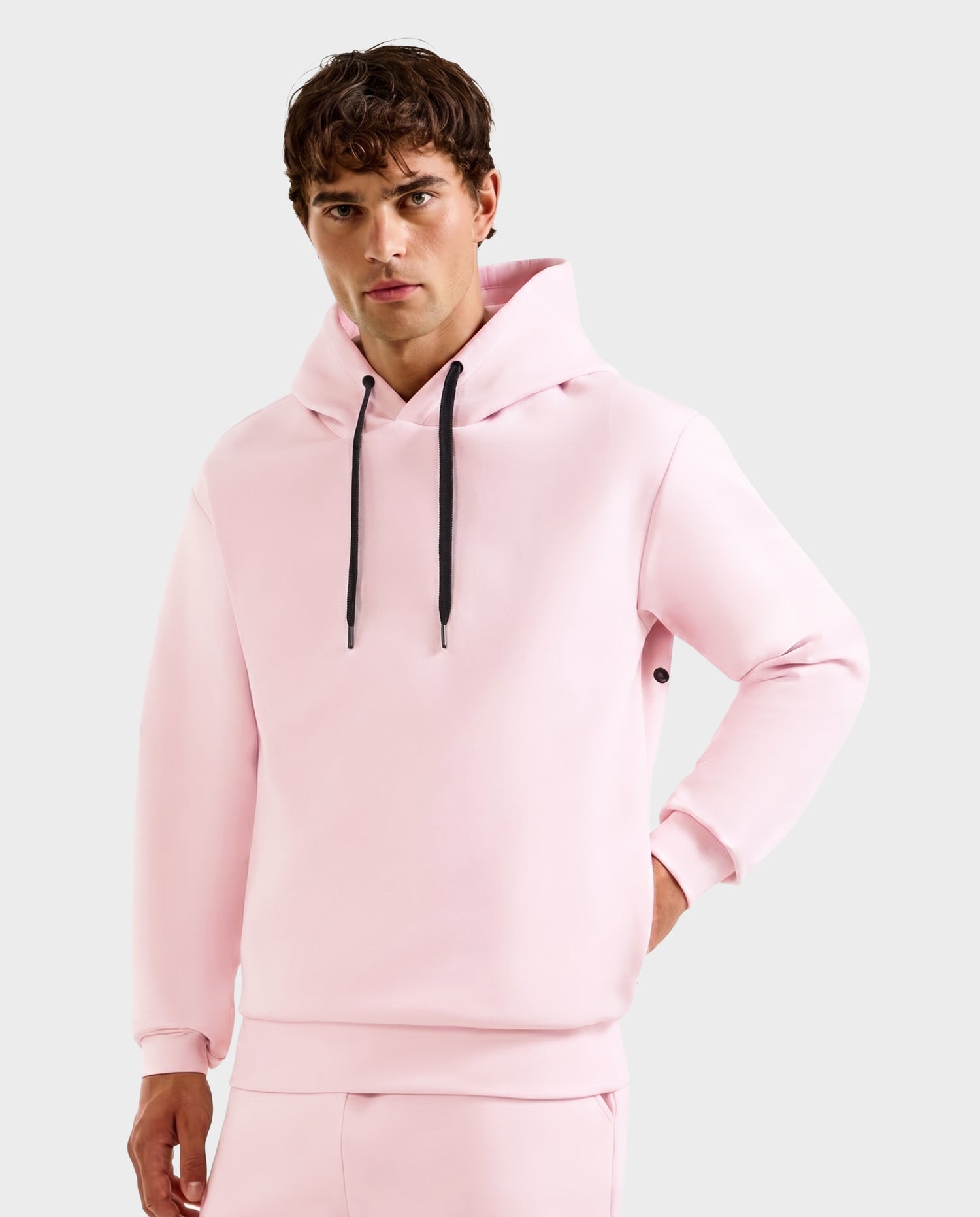 A man wearing the Rudsak LEROY - U525509 hoodie in light pink (size M) with black drawstrings and matching pants stands against a plain light gray background.