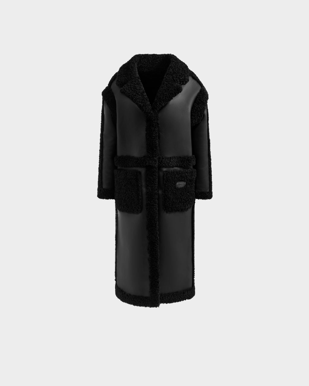 The Rudsak PALOMA - 8125675 Black is a long black faux shearling coat with a wide textured collar and lapels, matching trim, two large front pockets, and a straight silhouette shown against a plain light background.