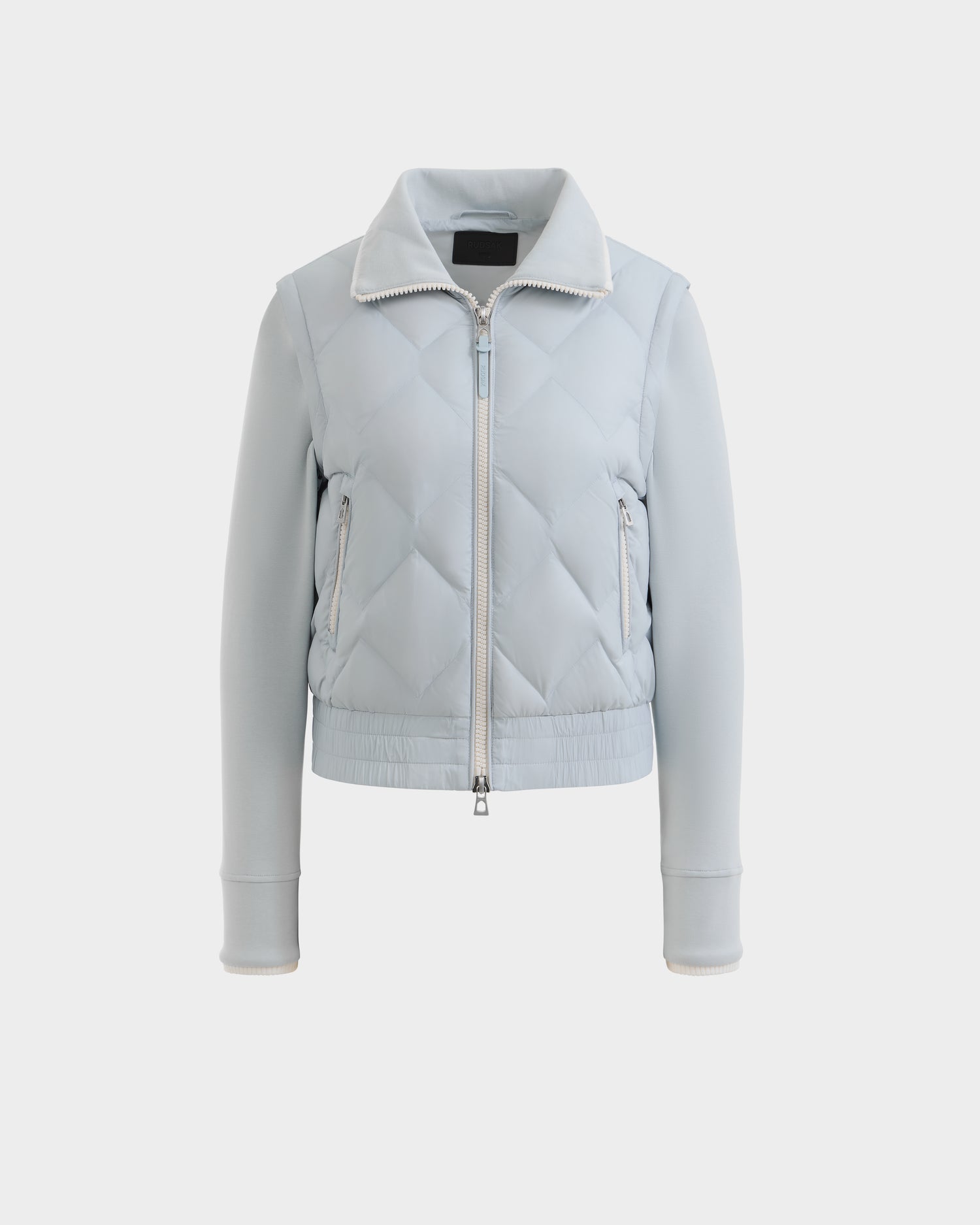 The Rudsak PRISA - 8126022 Powder Blue is a light blue convertible down jacket with a front zipper, high collar, long sleeves, ribbed cuffs and hem, zipped side pockets, and removable sleeves for versatile styling. Shown on a white background.
