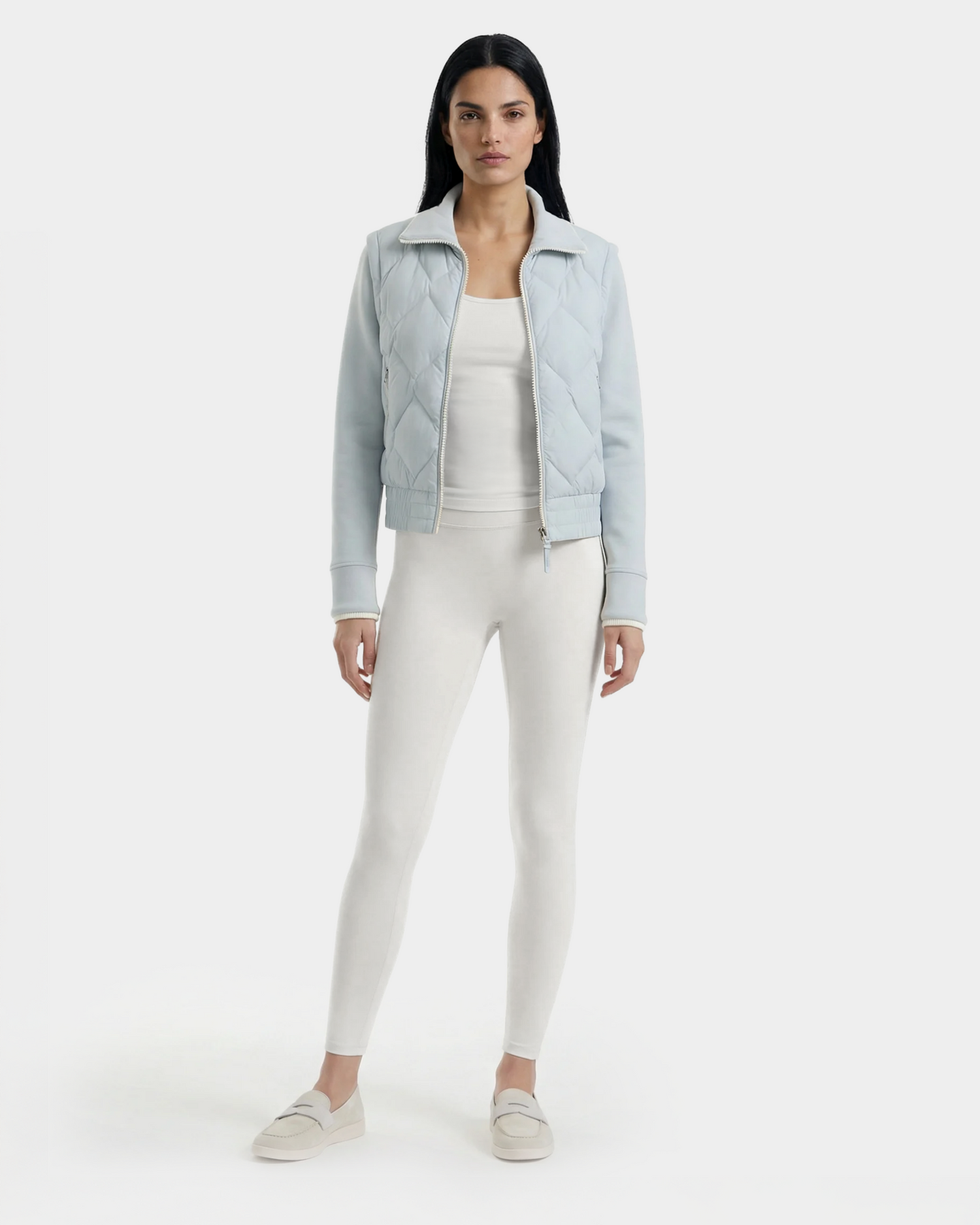 A woman faces forward in a Rudsak PRISA - 8126022 Powder Blue quilted jacket with removable sleeves, worn over a white top and leggings, paired with light slip-on shoes, set against a plain white background.