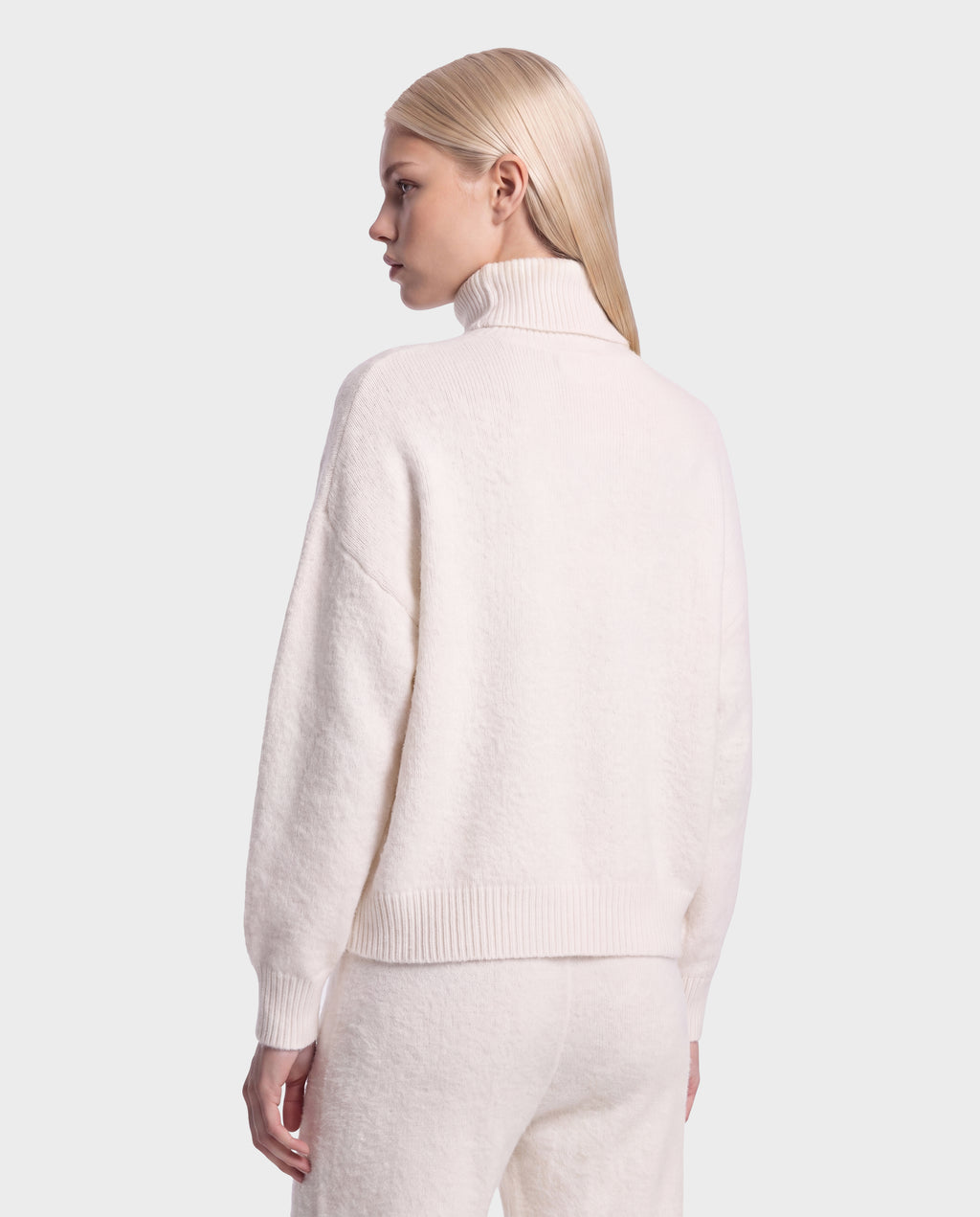 A person with straight, blonde hair is seen from behind, wearing the Rudsak ALISYA - 8526505 Iceland fuzzy knit turtleneck sweater and matching pants in a relaxed silhouette, set against a plain light background.