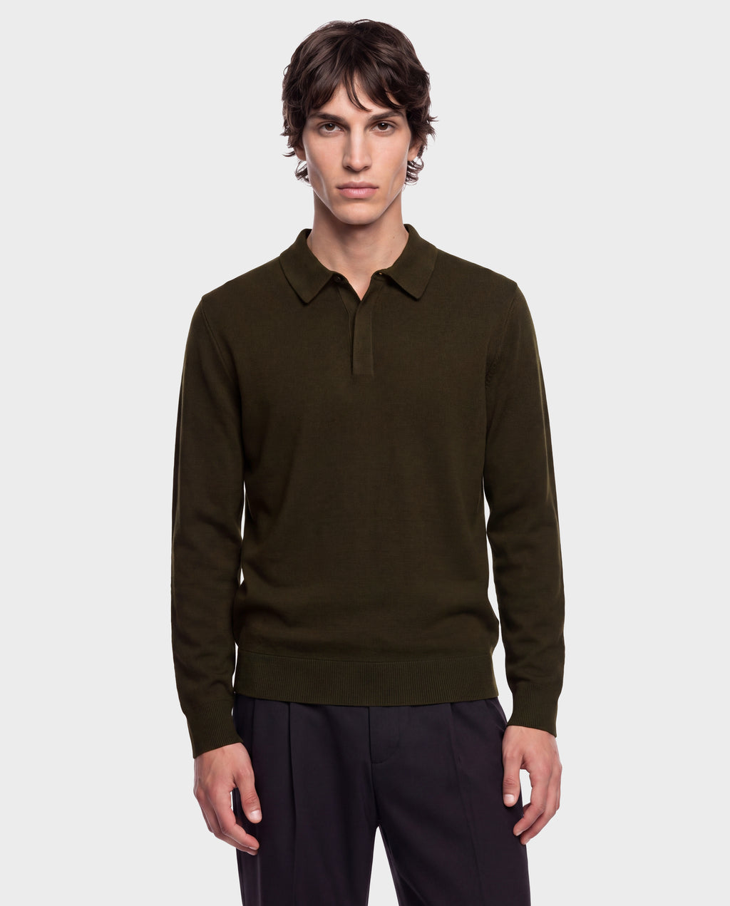 A young man stands facing forward with a neutral expression against a plain light gray background, wearing the Rudsak RICHARD - 6524529 Olive men’s knit polo sweater and black pants.