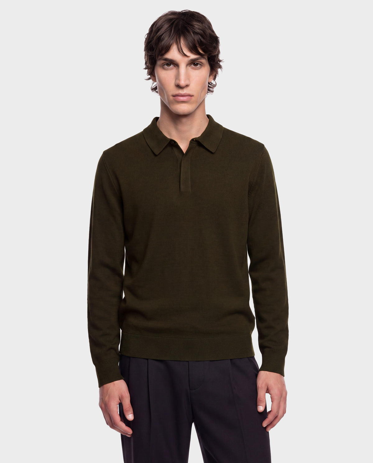 A young man stands facing forward with a neutral expression against a plain light gray background, wearing the Rudsak RICHARD - 6524529 Olive men’s knit polo sweater and black pants.