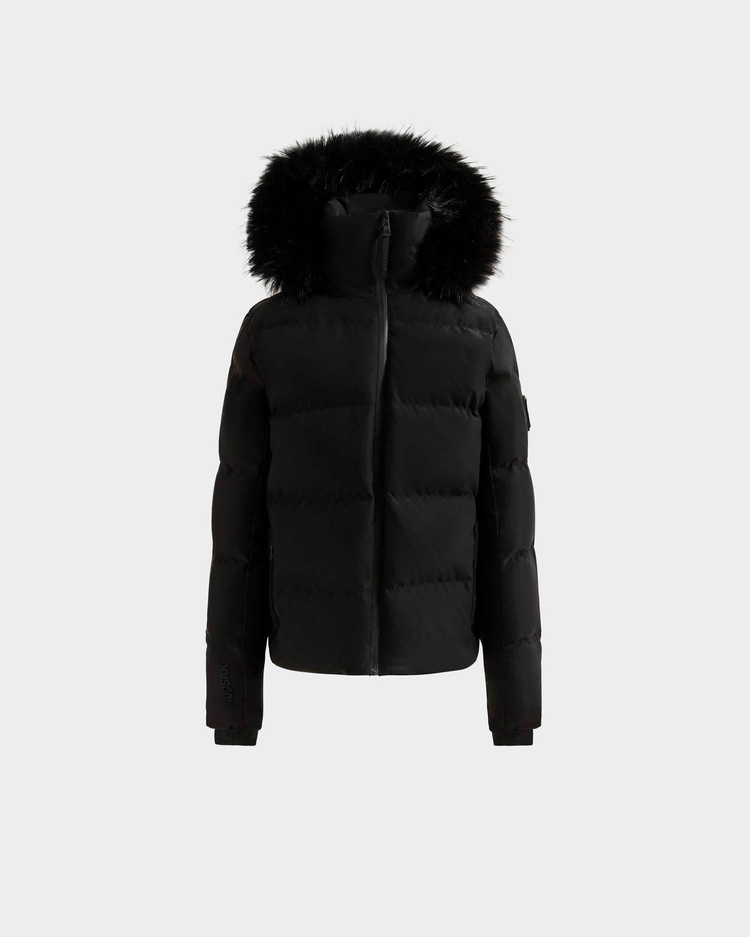 The Rudsak RAEGAN - 0125503 Black puffer jacket features a front zipper, long sleeves, and a large hood with black faux fur trim, shown against a plain white background.