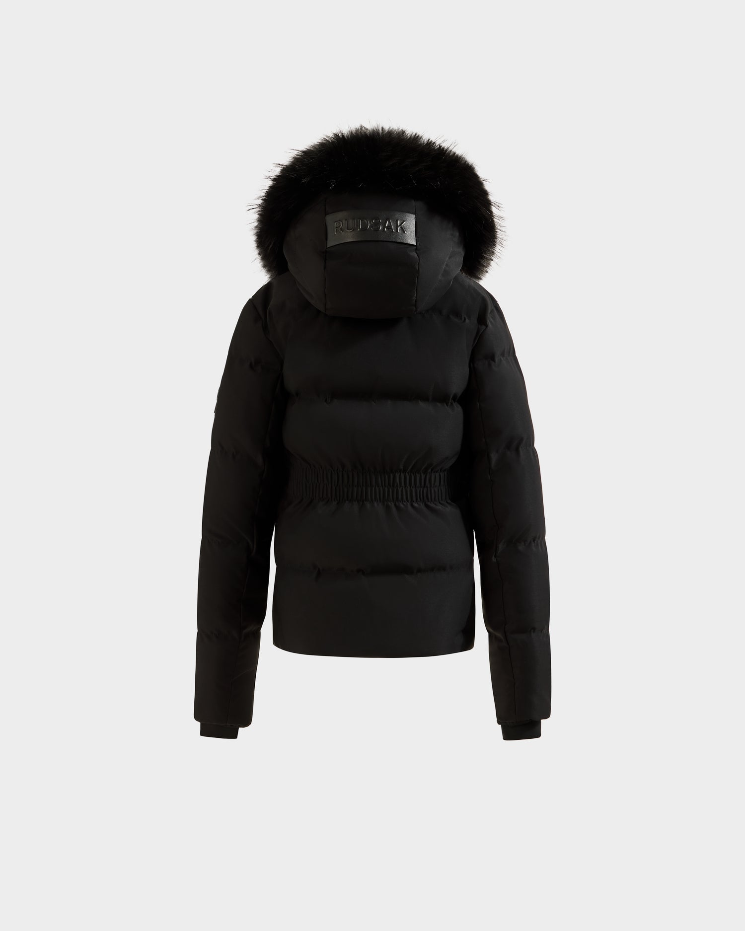 The Rudsak RAEGAN - 0125503 Black is a black, padded winter jacket with a fur-trimmed hood, cinched waist, and long sleeves, displayed from the back against a plain white background.