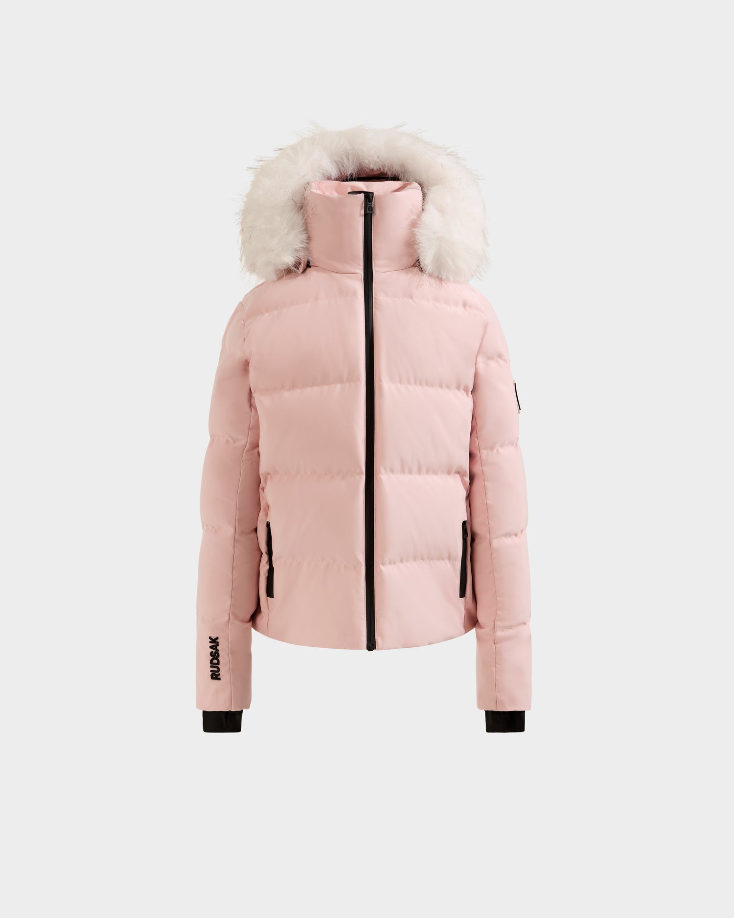 The Rudsak RAEGAN - 0125503 Pastel Pink is a light pink puffer jacket with a high collar, zip front, two zippered pockets, black sleeve cuffs, and a hood trimmed with white faux fur. Brand logos appear on the left sleeve and right wrist.