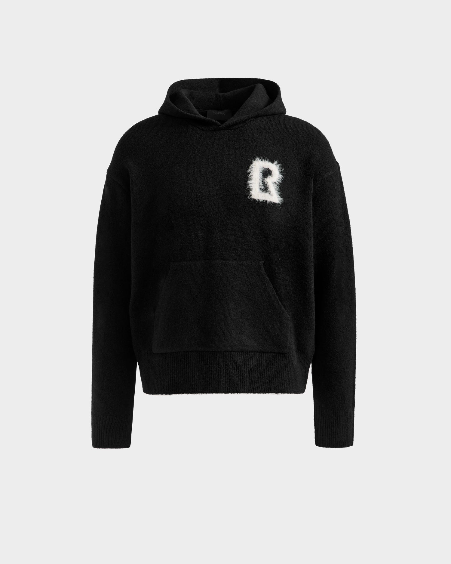 The RAPHAEL - 6525643 Black men’s hoodie by Rudsak features a kangaroo pocket and a white, fuzzy letter R patch on the left chest—ideal for upgrading your streetwear or loungewear. Shown against a plain light background.