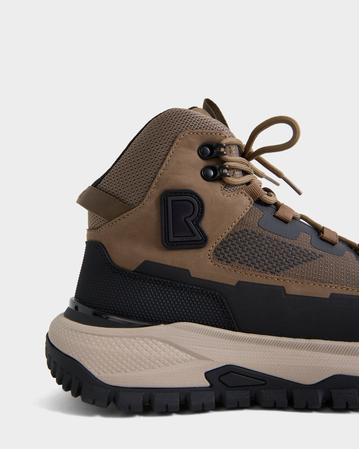 A close-up side view of the Rudsak REXON - 6226503 Cement high-top sneaker in brown and black, showcasing textured panels, mesh details, a rugged sole, and a prominent R logo on the side.