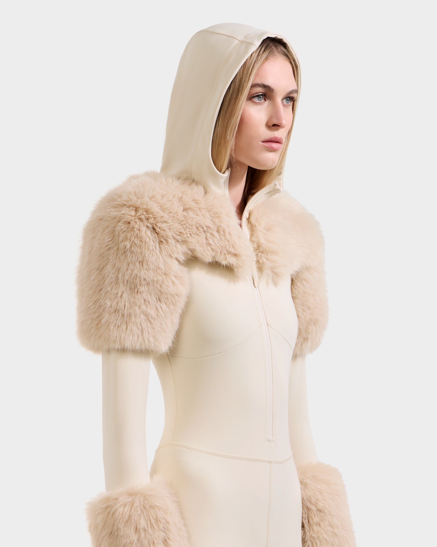 A woman models the Rudsak MYLA - 8525671 Vanilla bodysuit, featuring cream color and matching faux fur at the shoulders and sleeves, capturing an après-ski winter vibe against a white backdrop.