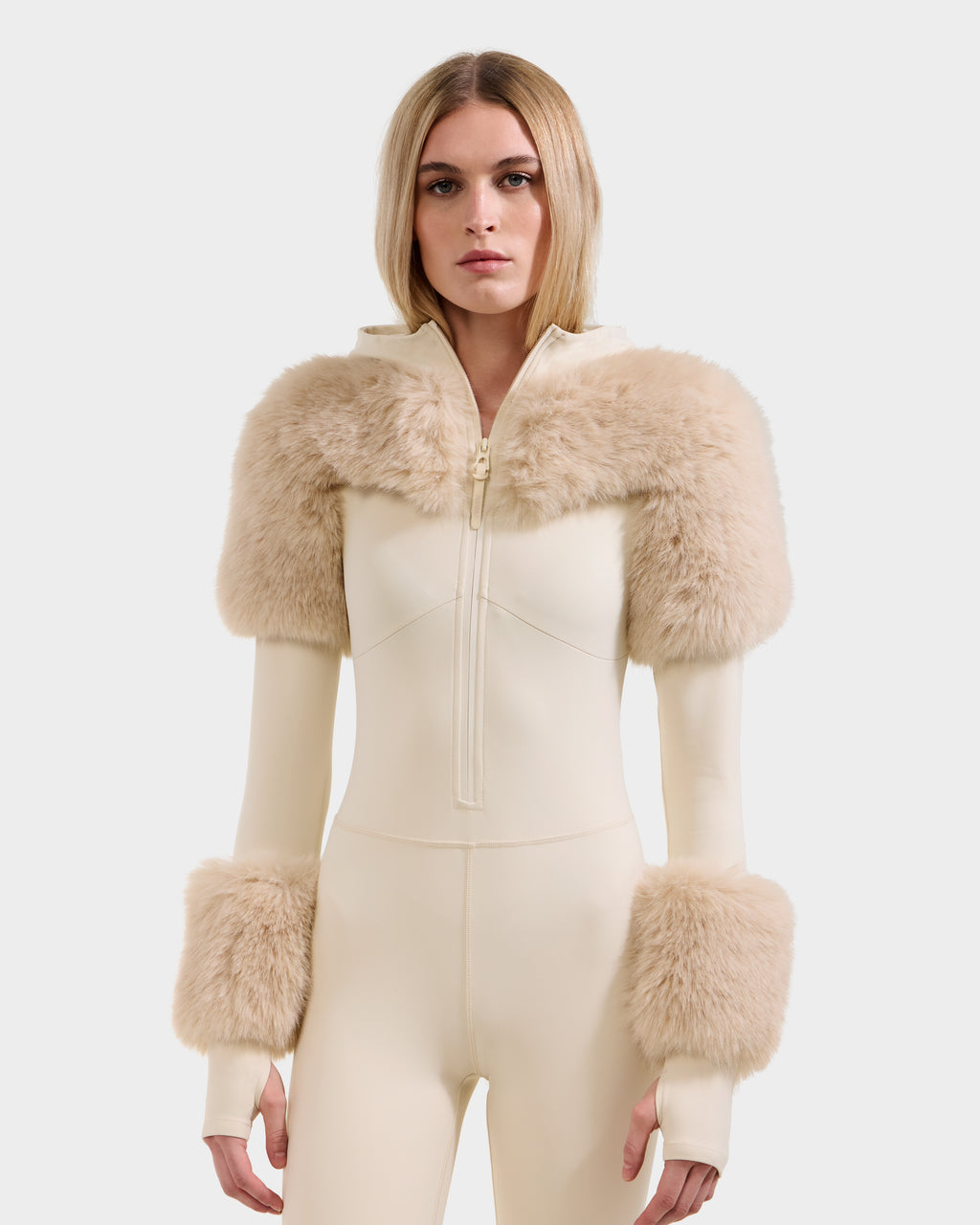 A woman models Rudsak’s MYLA - 8525671 Vanilla, a cream fitted one-piece bodysuit with zip front and beige faux fur accents, displaying chic winter style against a white background.
