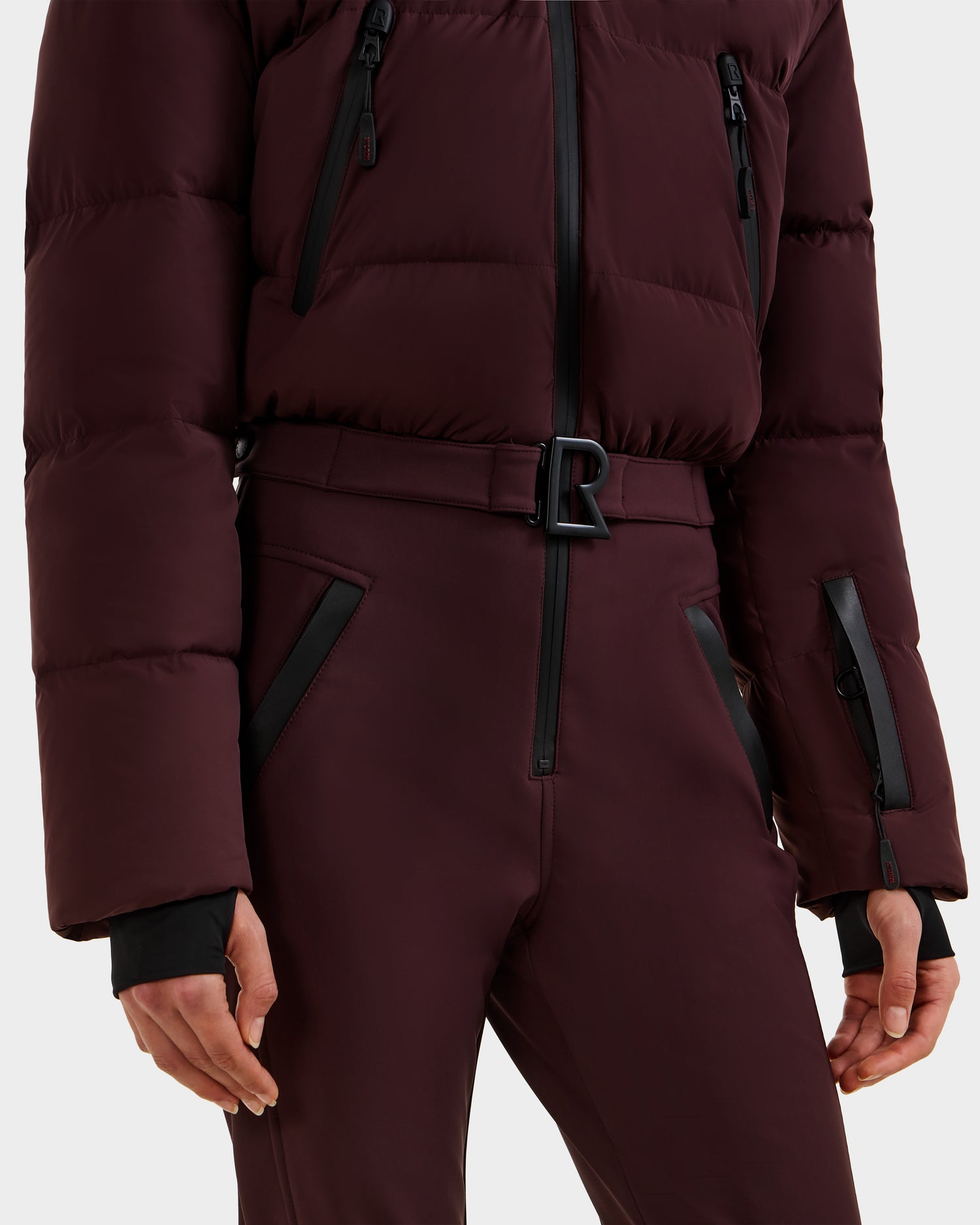 A person is shown from neck to mid-thigh wearing the Rudsak DINARA - 8125600 Bordeaux women’s ski suit, featuring matching high-waisted pants, black zipper details, and a belted waist.