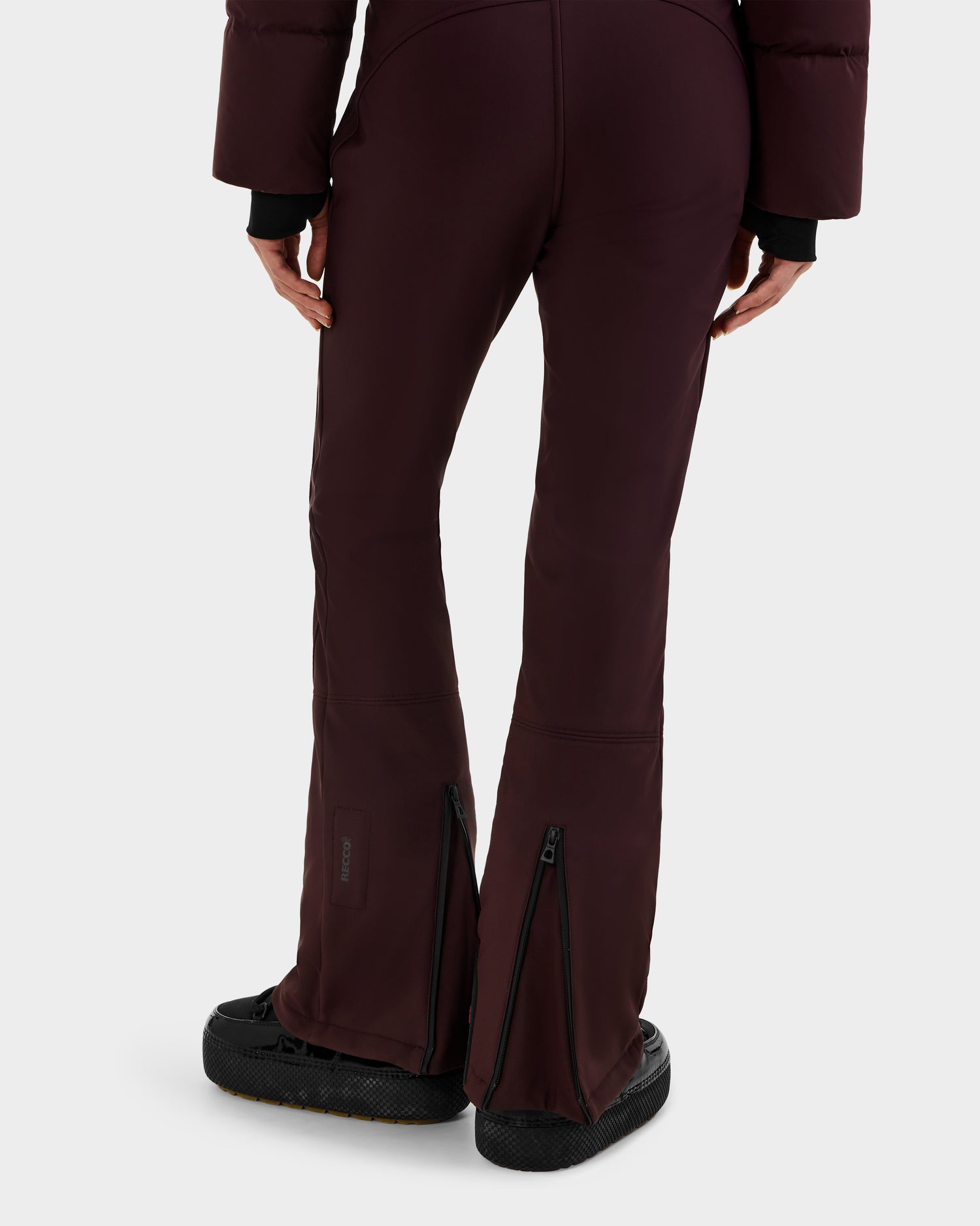 A person wearing Rudsak DINARA - 8125600 Bordeaux flared pants with visible back ankle zippers, paired with a matching jacket and black shoes, seen from behind against a plain backdrop—styled like a modern women's ski suit.