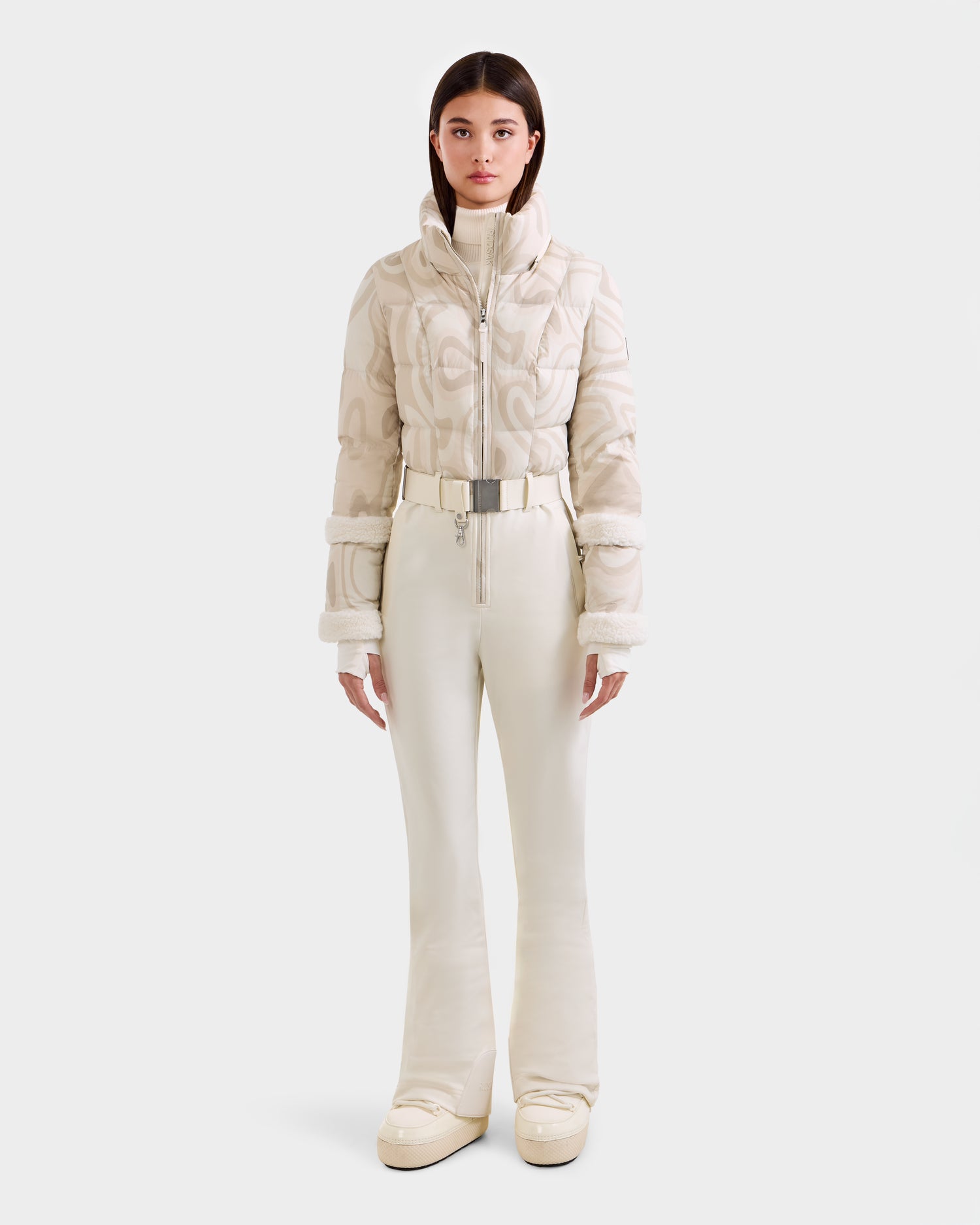 A woman faces forward in the Rudsak CARMEN P - 8125707 Vanilla Deja vu: a chic, cream ski outfit with quilted jacket, belted high-waisted pants, and platform boots. Pre-order now; ships by November 30th.