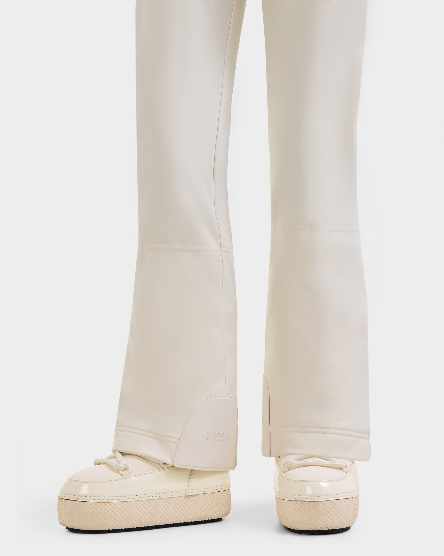 A close-up of a person wearing Rudsak’s CARMEN P - 8125707 Vanilla Deja vu cream pants and matching slip-on shoes with textured soles, set against a white background. Now available for pre-order, shipping by November 30th.