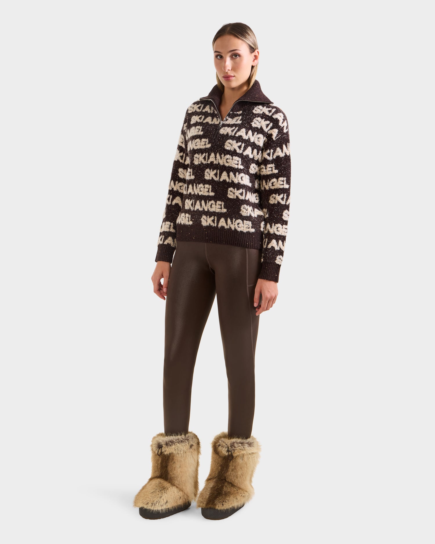 A woman wears the Rudsak LYDIA - 8525687 Espresso sweater with fitted brown pants and large tan fur boots, standing against a plain white background.