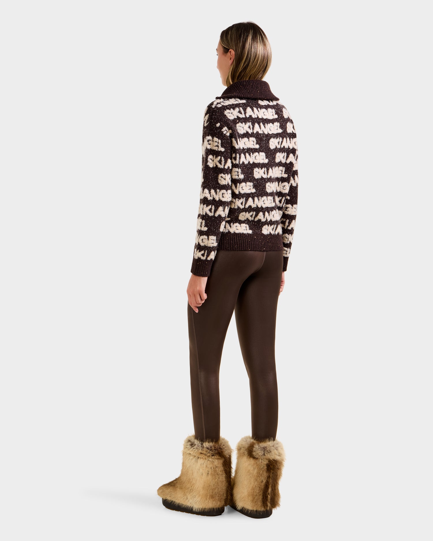 A person stands facing away, wearing the Rudsak LYDIA - 8525687 Espresso sweater—a women’s knit pullover—paired with brown leggings and tan furry boots, set against a plain white background.