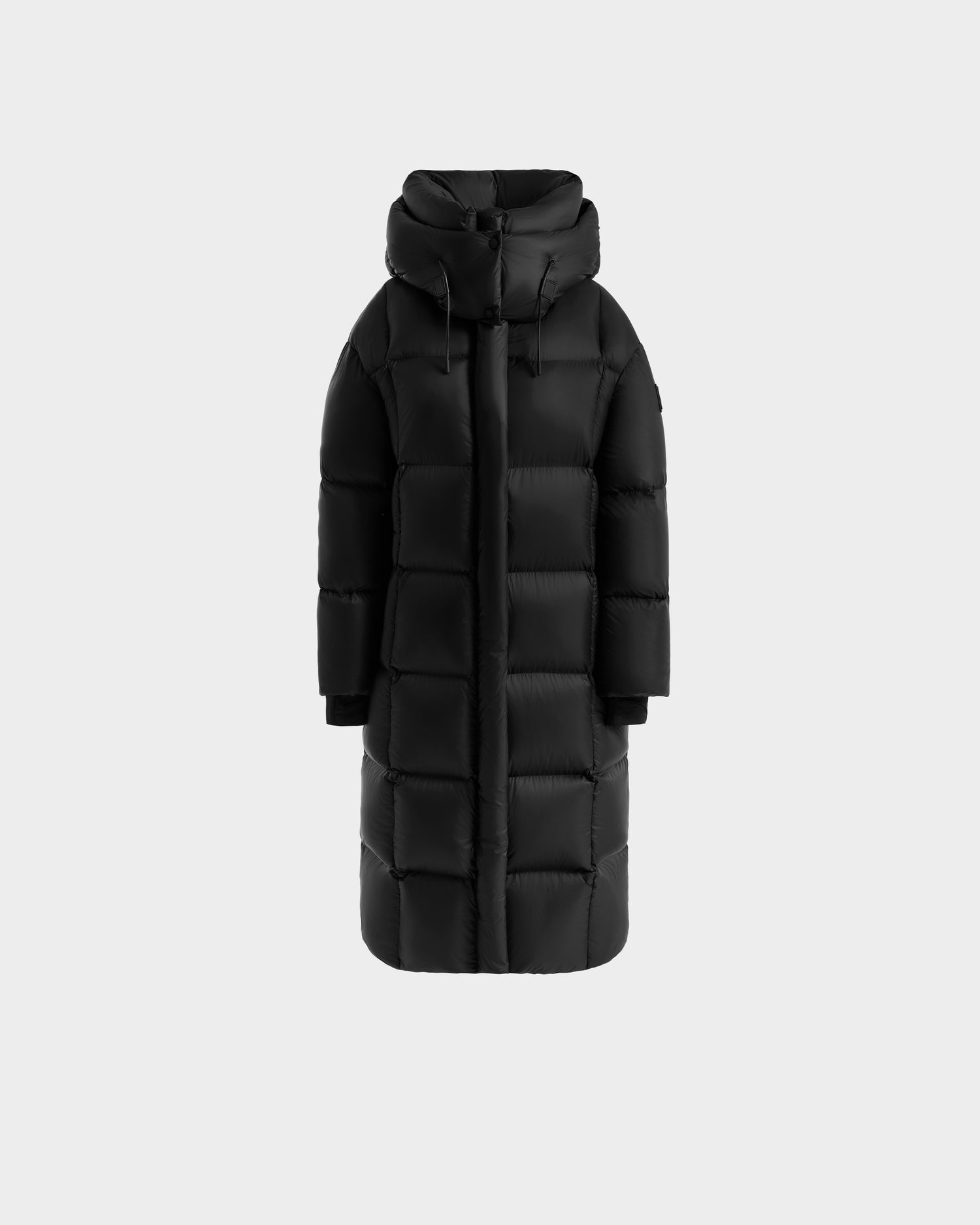 The Rudsak SASHA - 8125686 Black is a women’s long down puffer coat with RDS-certified down, a hood, front zipper, and square quilted pattern, shown against a plain light gray background.