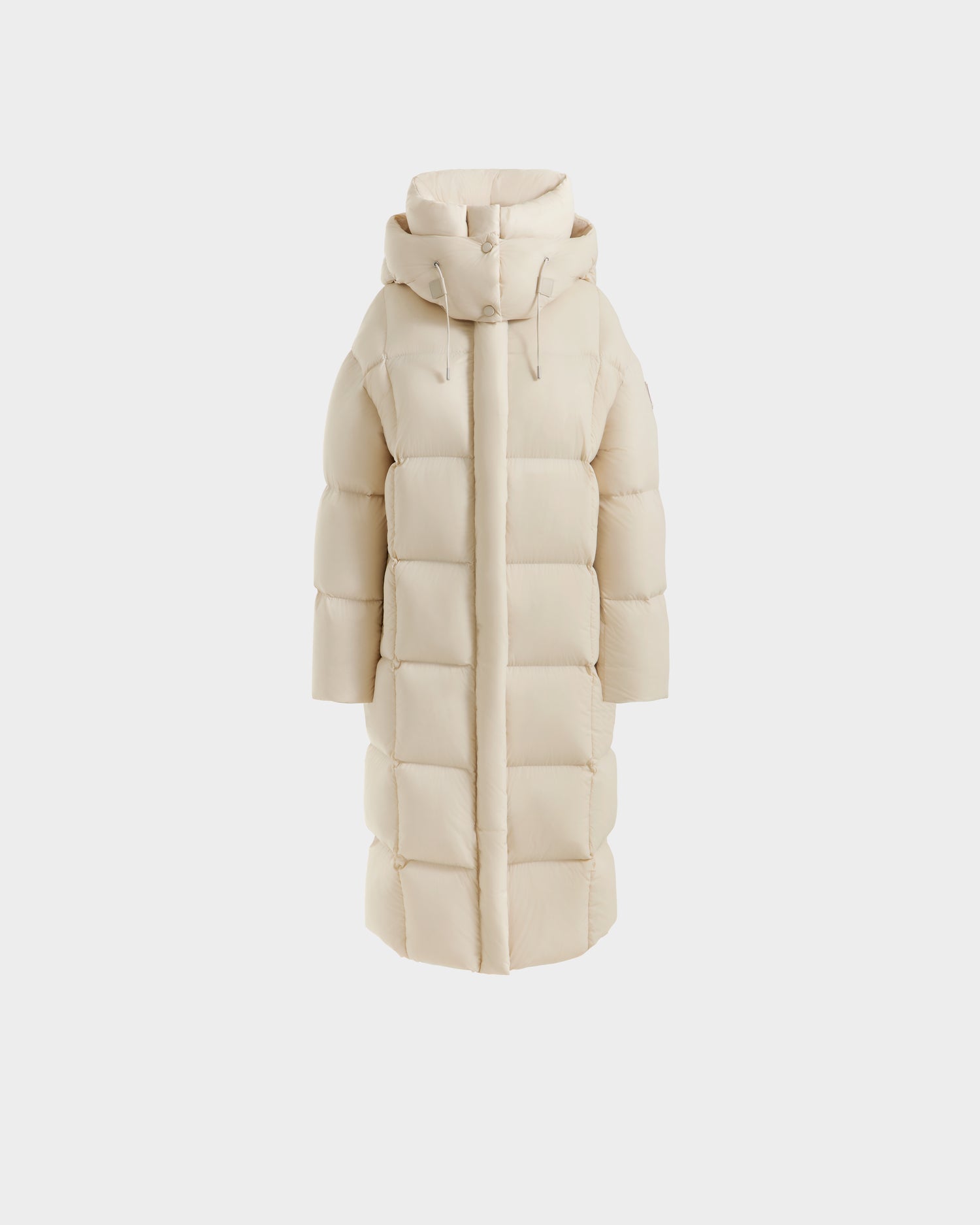 The Rudsak SASHA - 8125686 Vanilla is a women's long beige down puffer coat with a hood, front zipper, large horizontal quilting, and high collar, shown against a plain white background.