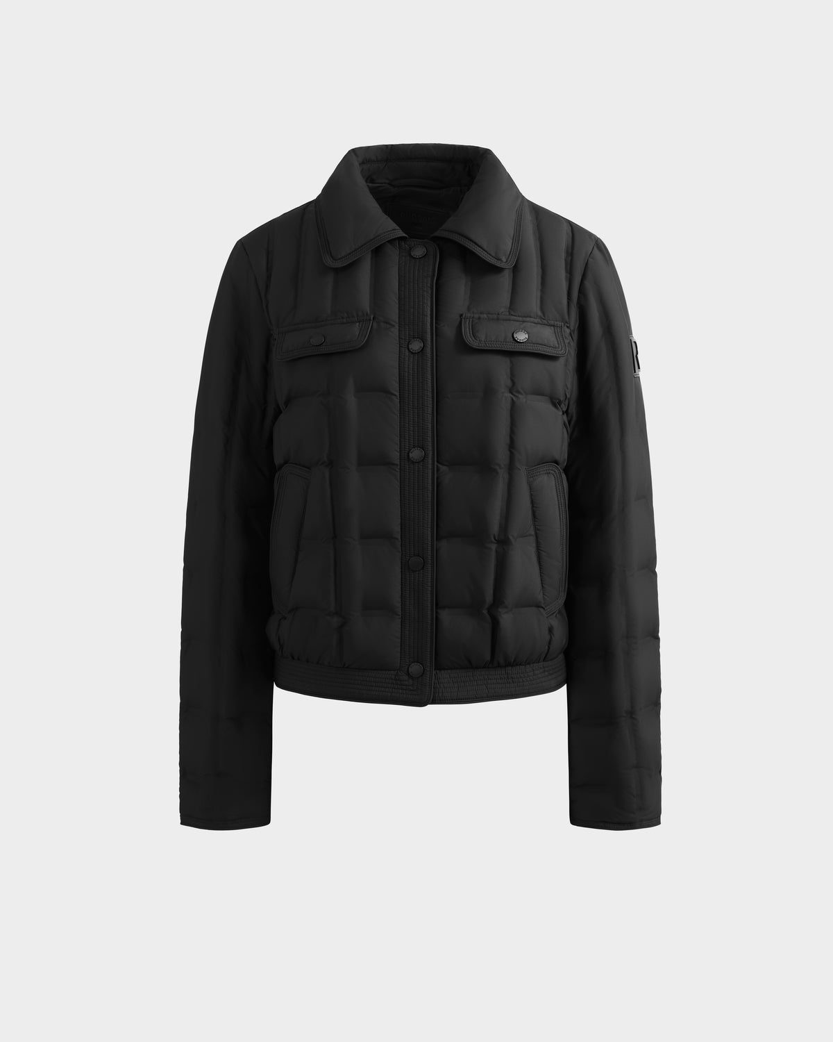 The Rudsak SEOUL - 8126027 Black is a quilted down jacket with RDS-certified duck down, a collar, snap button front, chest flap pockets, and long sleeves, shown on a plain light background.