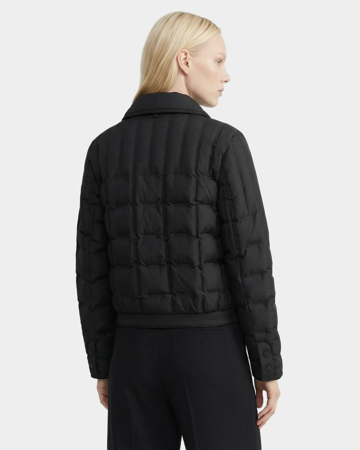 A person with straight, light blonde hair models the Rudsak SEOUL - 8126027 Black quilted down jacket and black pants, standing at a slight angle against a plain white background.
