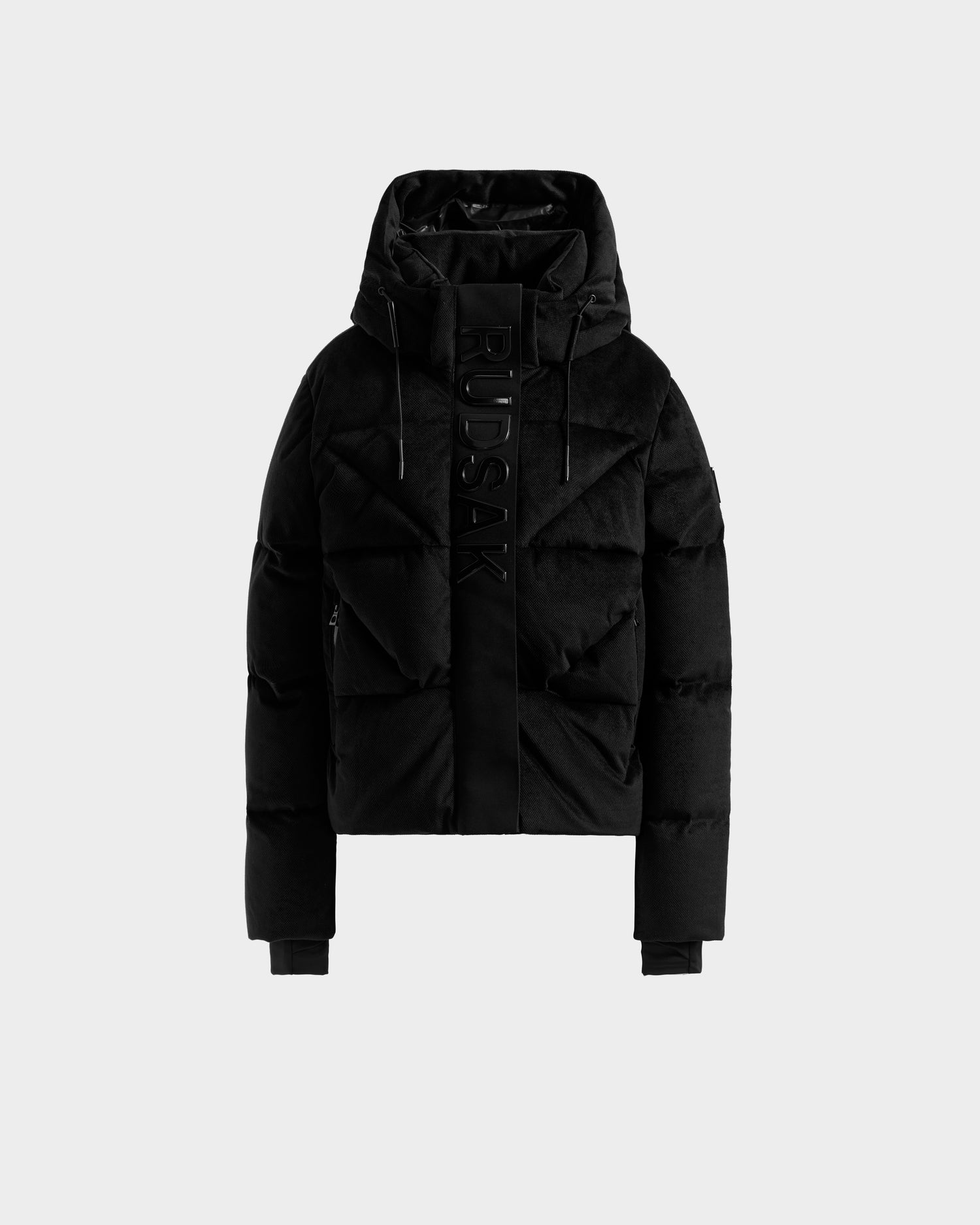 The STEFANIE V - L125584 Black by Rudsak is a warm, slightly cropped down puffer jacket with a hood, front zipper, ribbed cuffs, and "RUDSAK" embossed vertically on the left front side. Displayed on a plain white background.