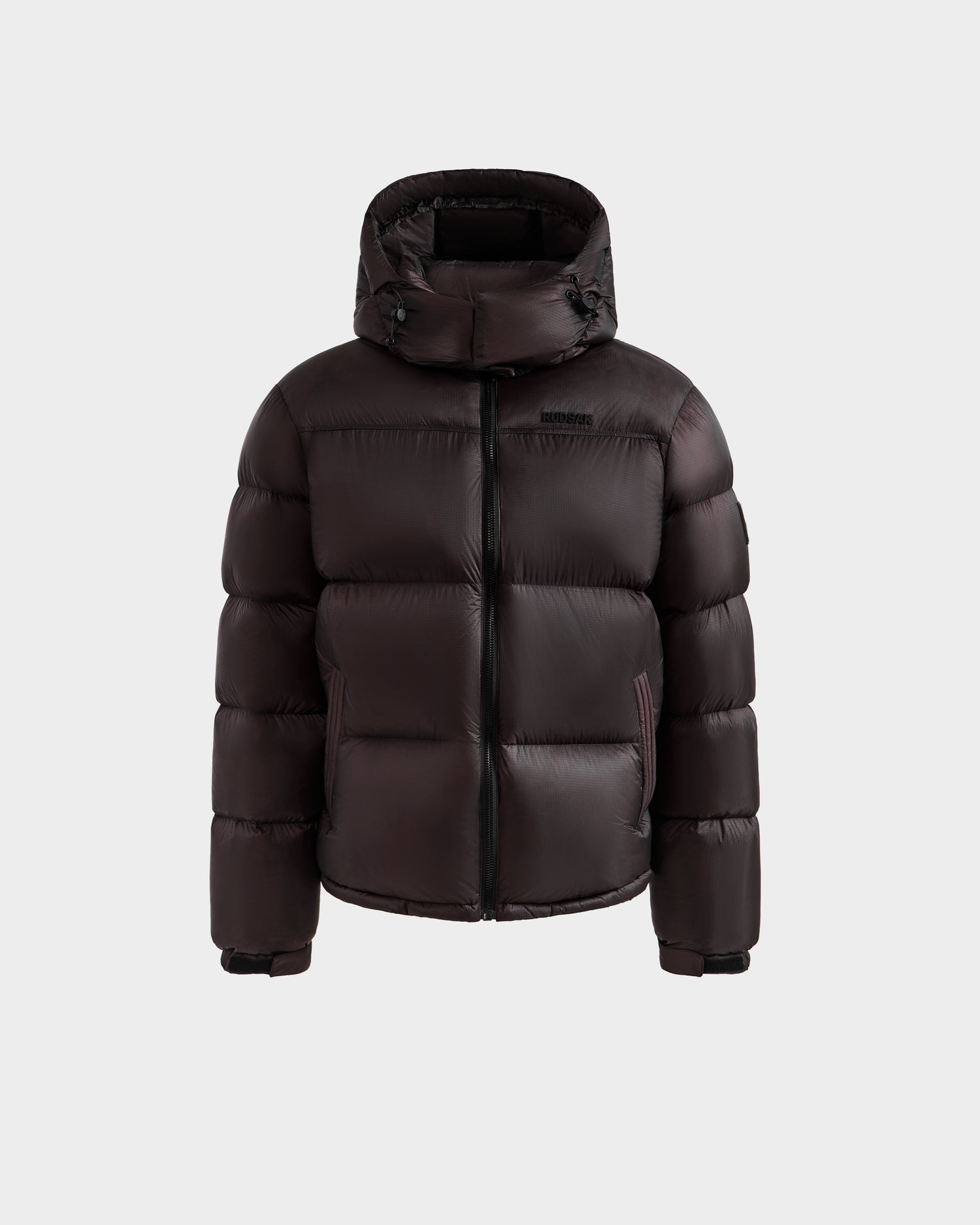 The STEFANO - 6125574 Espresso by Rudsak is a men’s dark brown down puffer winter jacket with a hood, front zipper, and two side pockets, shown against a plain light gray background.