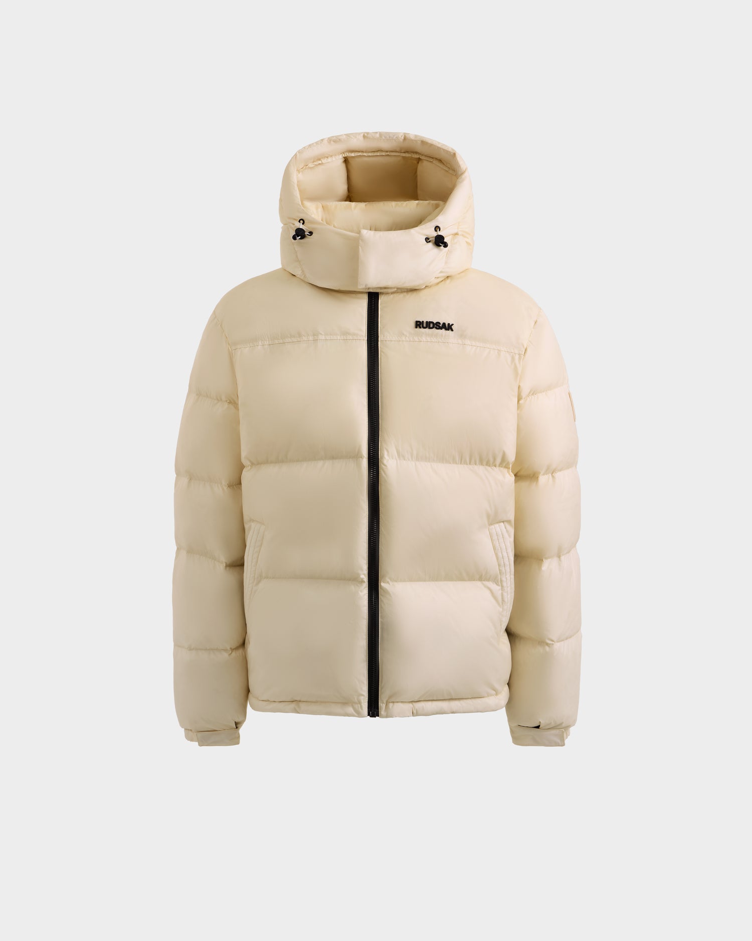The STEFANO - 6125574 Vanilla by Rudsak is a cream-colored men’s down puffer jacket with a hood, black zipper, RUDSAK branding on the left chest, and RDS-certified down, shown on a plain white background.