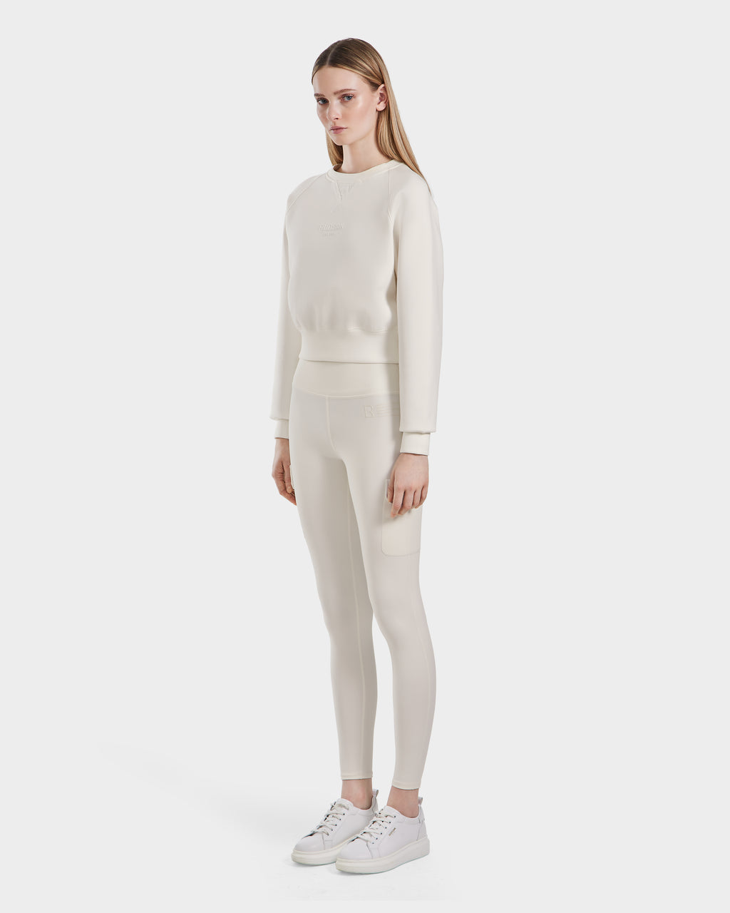 A woman faces forward, wearing the Rudsak BETSY - 8525087 Iceland matching cream premium cotton blend crewneck sweater and leggings set with white sneakers, against a plain white background.