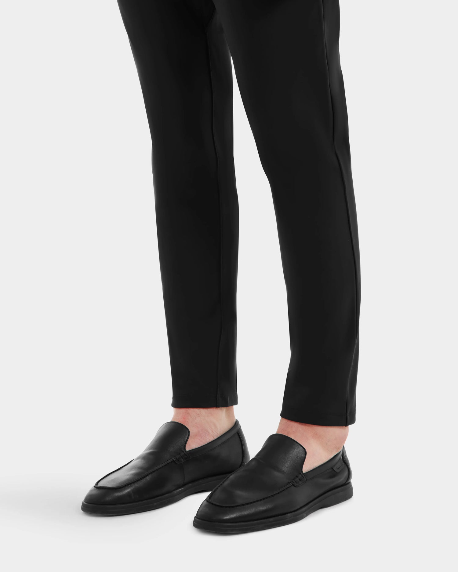 A person wearing Rudsak’s CHANNING - 6225005 Black premium men’s leather loafers and black tapered pants stands on a plain white background.