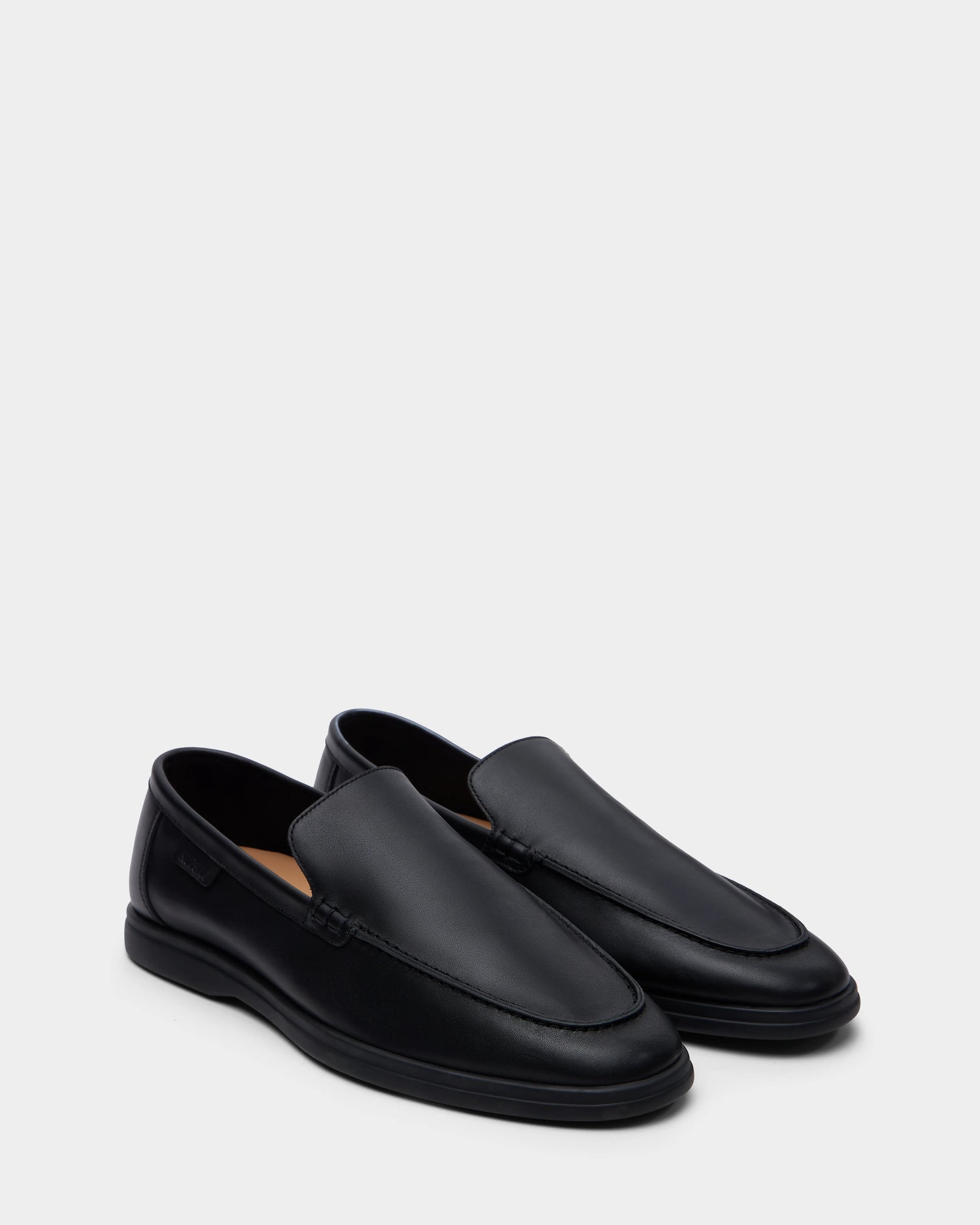 The CHANNING - 6225005 Black by Rudsak are premium men’s black leather slip-on loafers with a sleek minimalist design, rounded toes, and subtle edge stitching, shown on a plain light gray background.