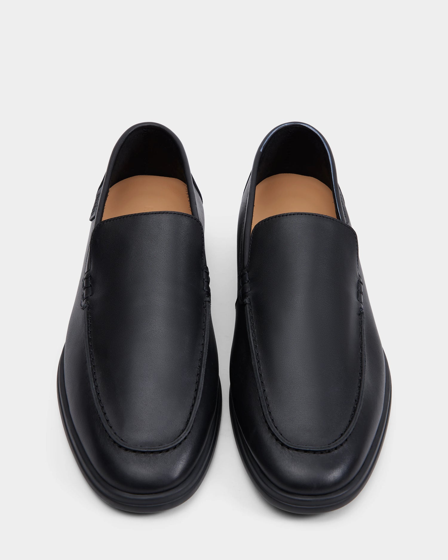 The Rudsak CHANNING - 6225005 Black features black slip-on loafers with rounded toes, tan interiors, and visible stitching, shown side by side on a light gray background—perfect for those seeking premium men’s footwear.