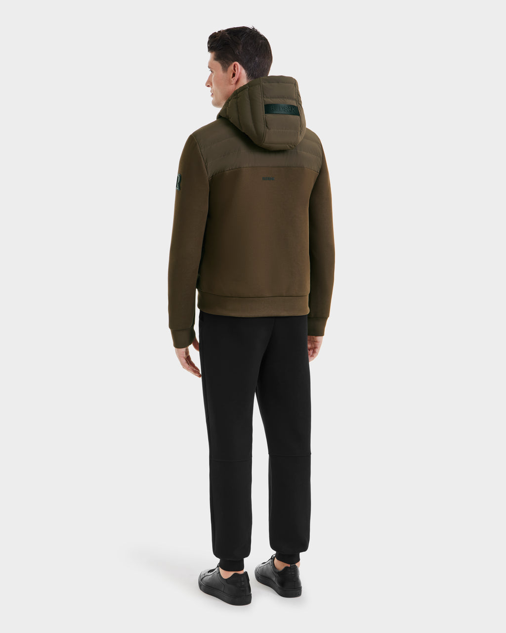A man, facing away, wears the Rudsak DEE MAT - 6124028 Army mens lightweight hybrid down jacket with black pants and sneakers against a plain white background.