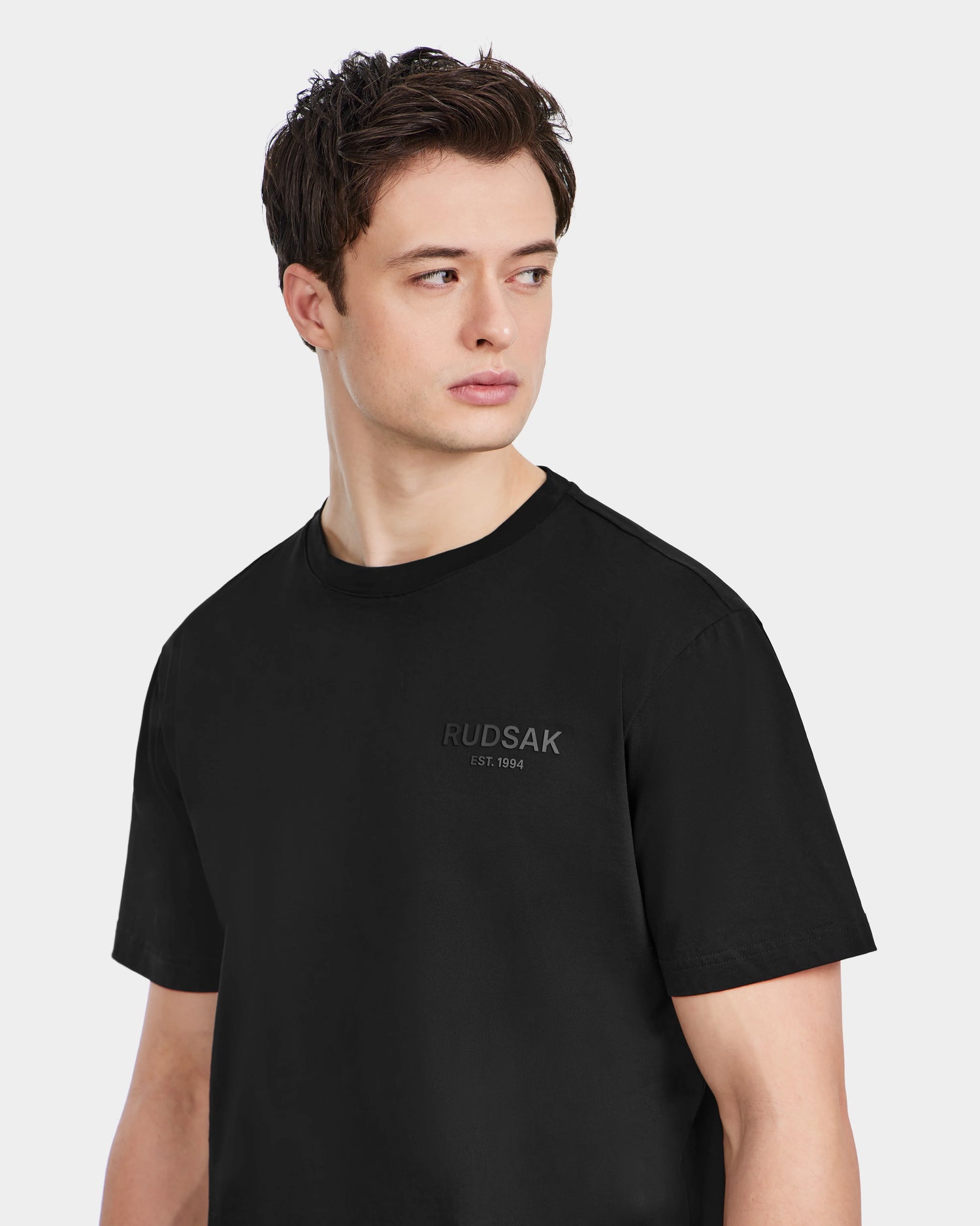 A man in the Rudsak GRANT - 6525036 Black crewneck tee made from premium cotton looks to the side.