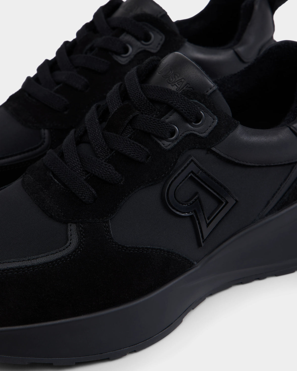Close-up of Rudsaks LIONEL - 6225001 Black mens sneaker, featuring a thick sole, raised embossed logo, and a modern mix of suede and smooth materials—combining style and durability for everyday wear.