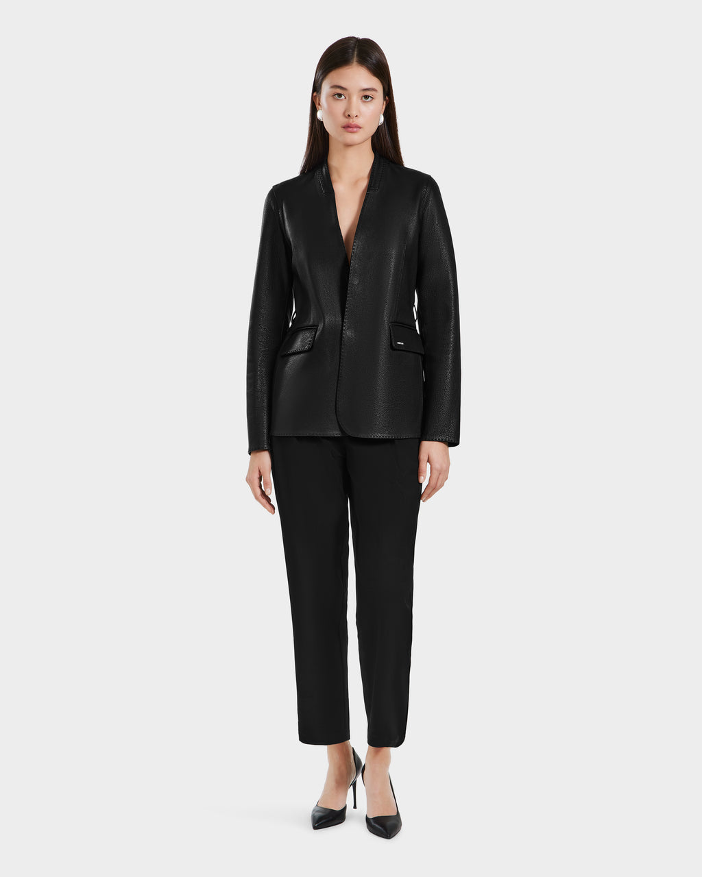 A woman faces forward against a plain white background, wearing the Rudsak PAMILA - 8125051 Black blazer and black pants, paired with pointed-toe heels for a minimalist, sophisticated look.