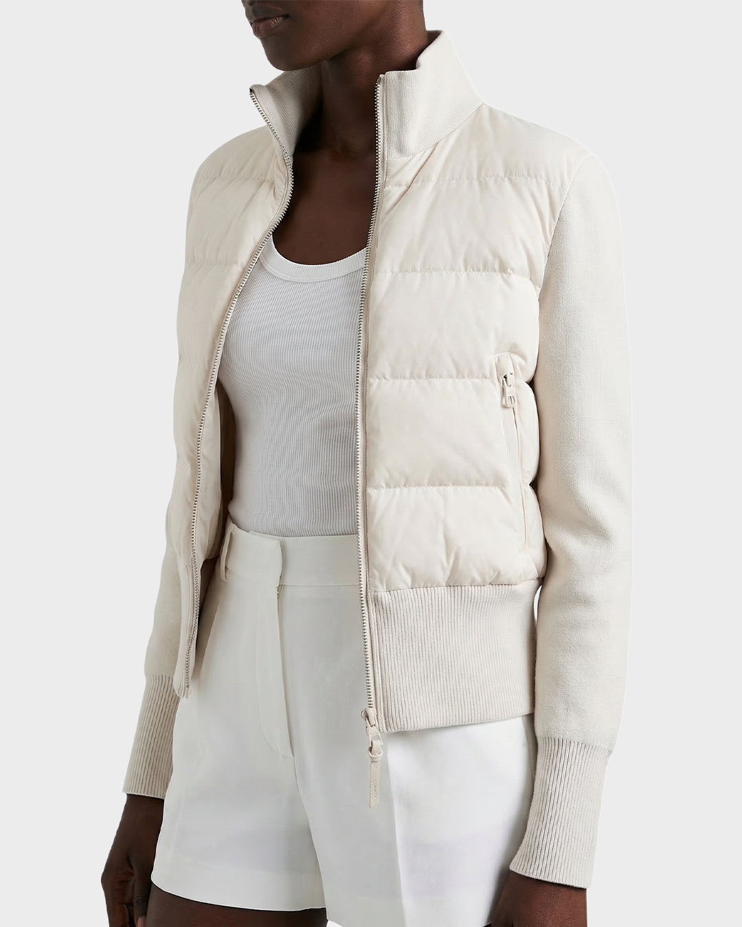 A model wears the Rudsak CLAREMONT - 8125502 Vanilla women's hybrid down jacket in light beige quilted fabric, over a white tank top and shorts, delivering lightweight warmth with RDS-certified down.