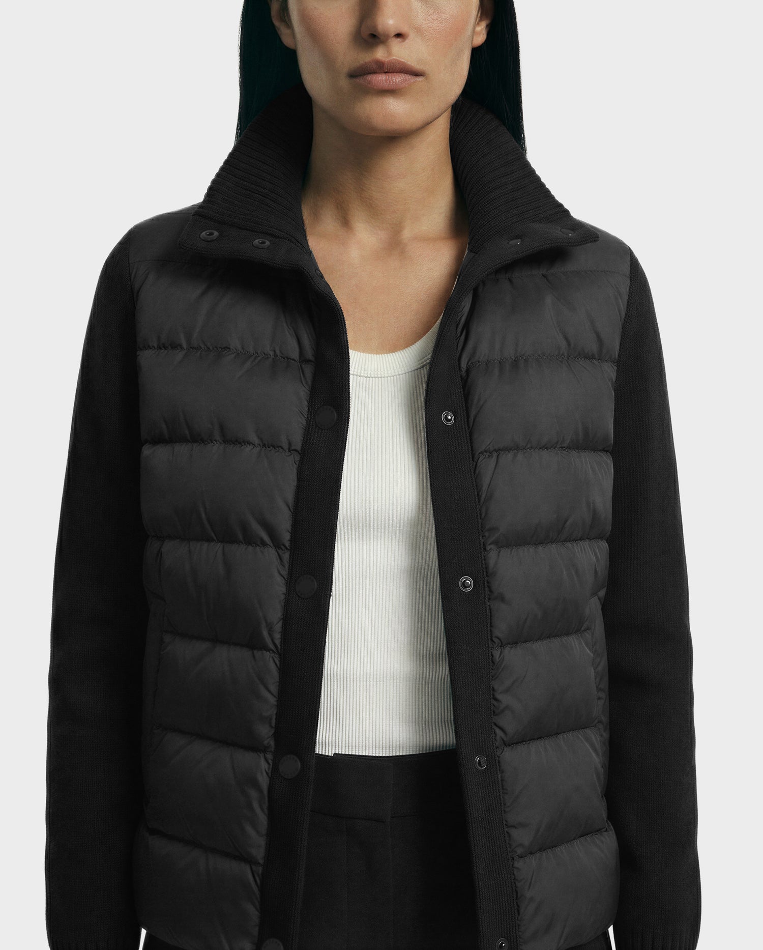 Showcasing transitional layering, a person wears the Rudsak ELLIE - 8125635 Black women's quilted down jacket with ribbed sleeves over a white ribbed tank top and black pants, pictured from shoulders to hips against a plain background.