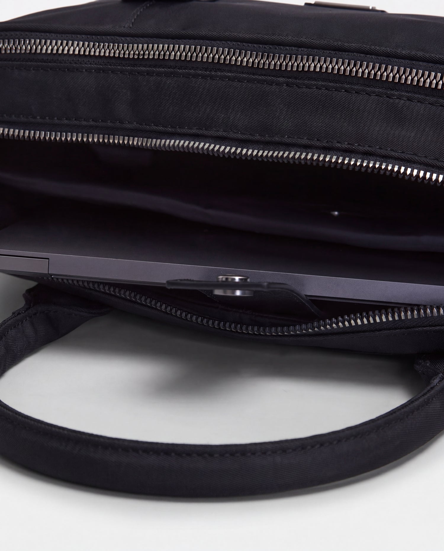 A close-up of the open Rudsak HENRY N - 9326056 Black laptop bag with a laptop partially visible inside, highlighting the zipper, handles, and inner compartments.
