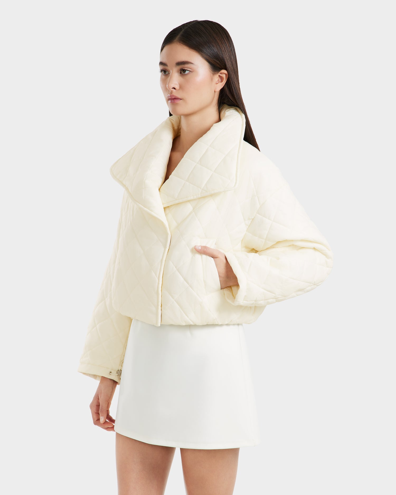 A woman wearing the Rudsak KALEE - 8124005 Iceland quilted light jacket with wide lapels and a matching short skirt stands against a plain light background.