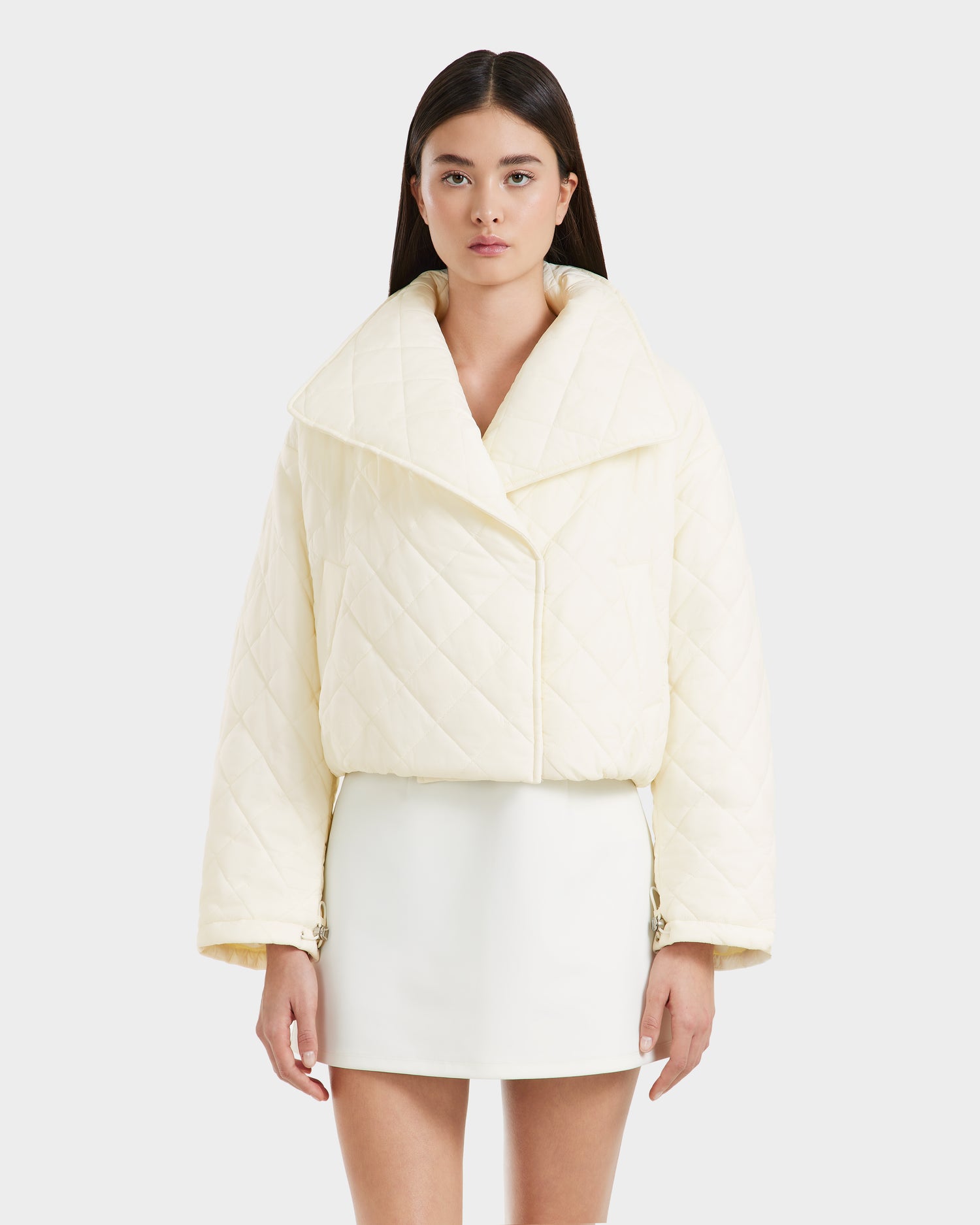 A woman stands facing forward wearing the Rudsak KALEE - 8124005 Iceland women's quilted light jacket with a wide collar and a matching white mini skirt against a plain light background.