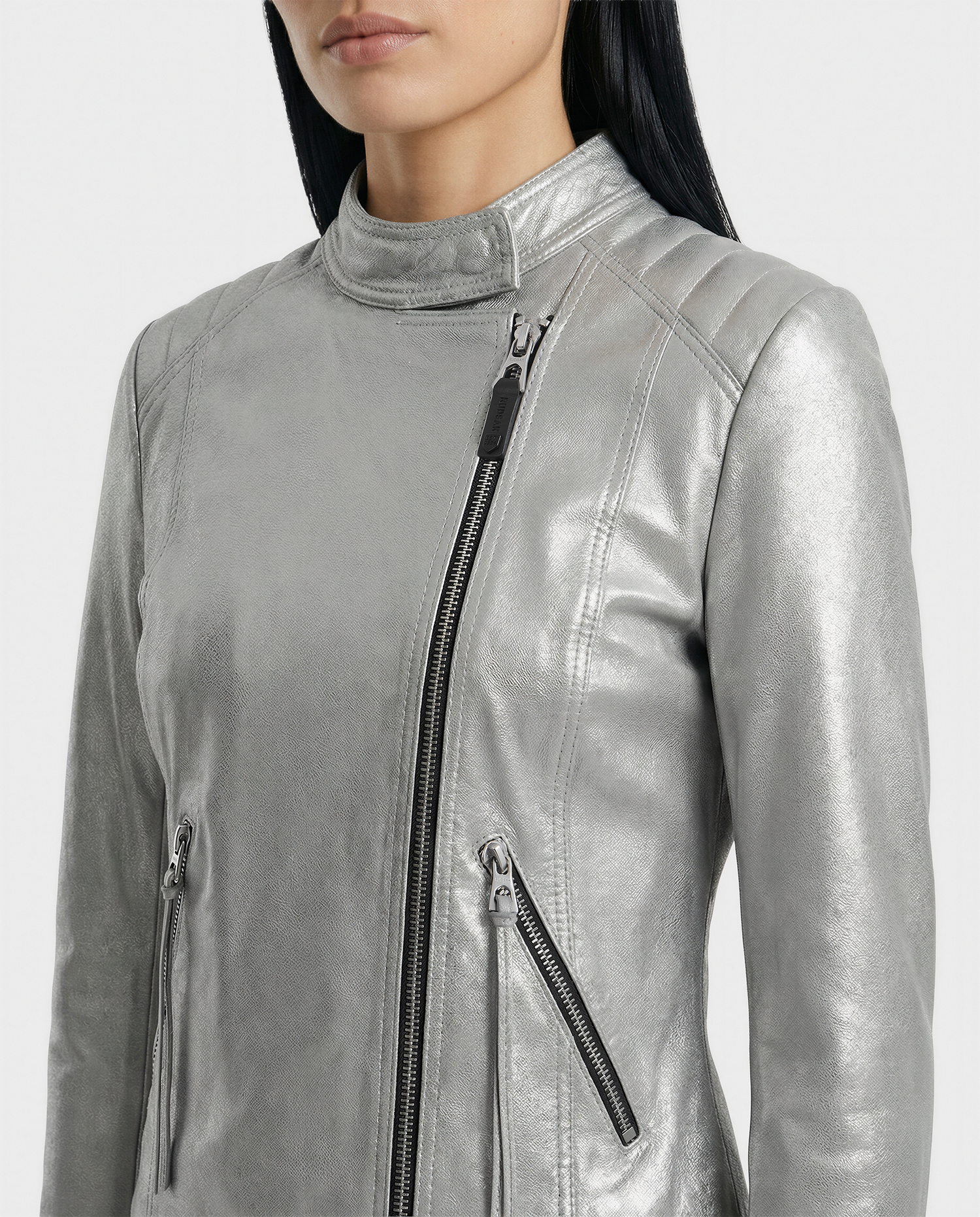 A cropped image shows a woman in the Rudsak MERINA - L120013 Metallic Aluminium jacket, featuring a shiny silver moto style, asymmetrical front zipper, and two slanted zippered pockets.