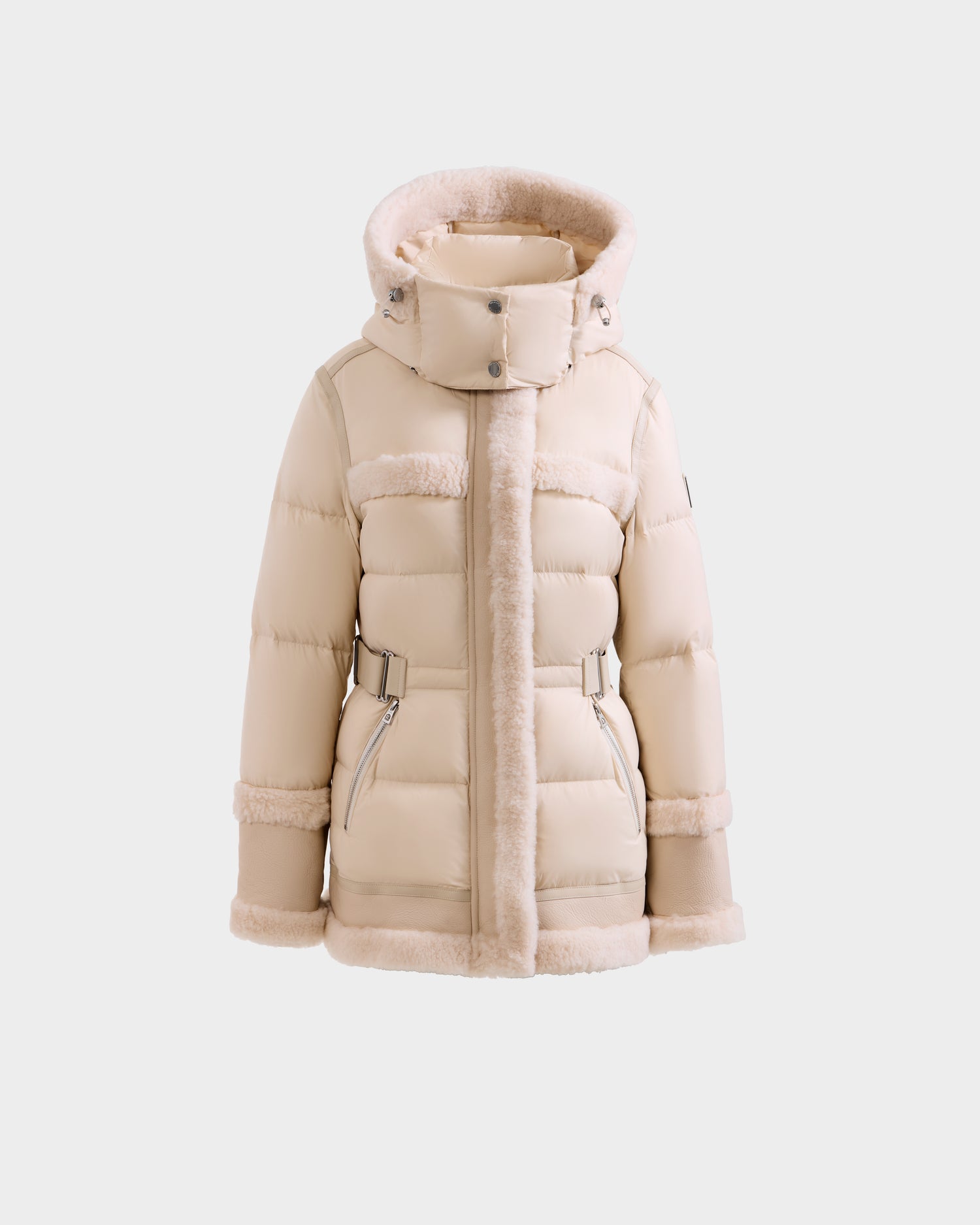 The Rudsak TESSA - 8125615 Vanilla is a cream women’s down puffer jacket featuring a hood with faux fur trim, front zipper, two zippered pockets, and belted details at the waist and cuffs for a stylish, cozy winter look.