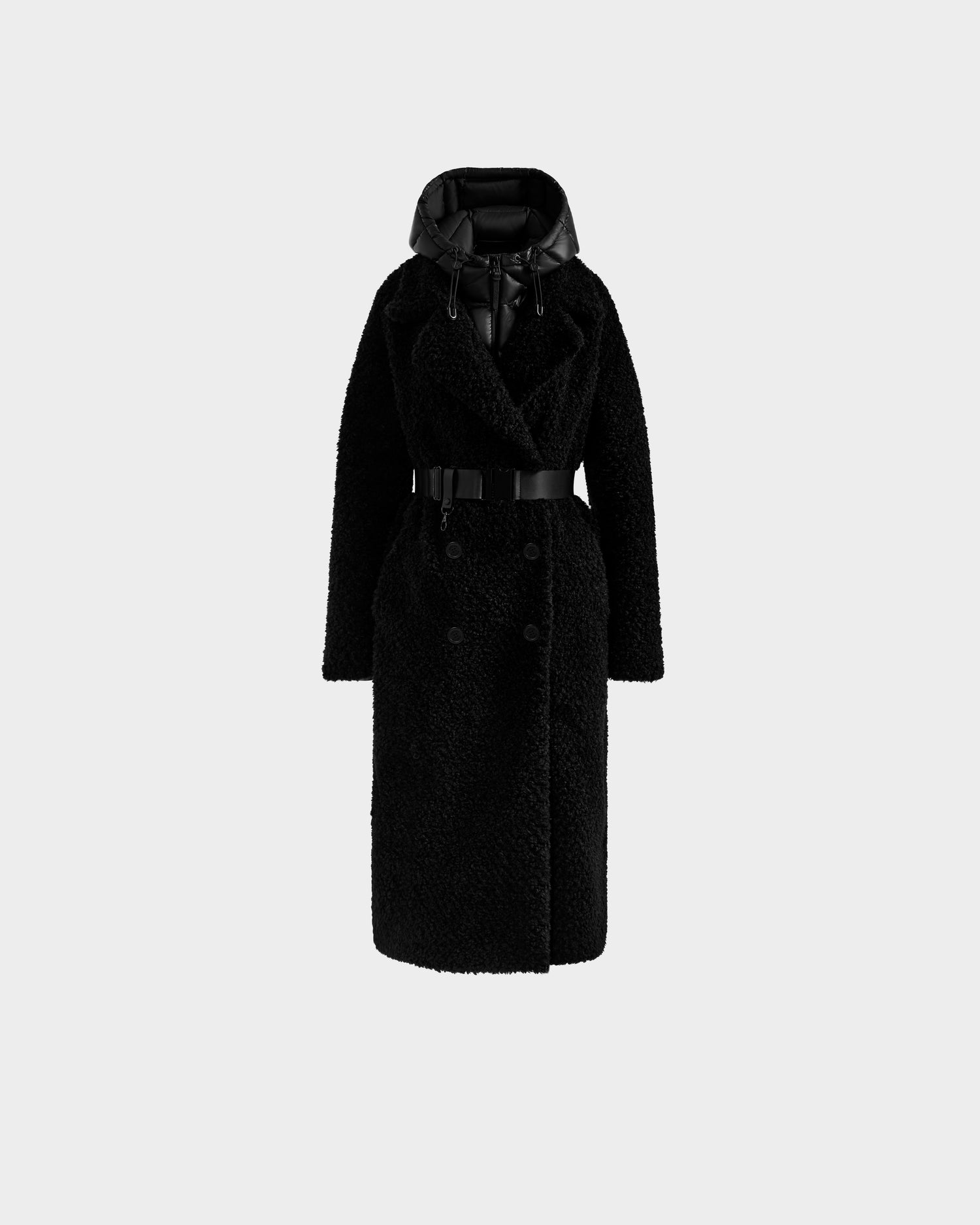 The Rudsak TINA - 8125968 Black is a women's long black textured faux fur coat with a wide collar, double-breasted buttons, belted waist, and a shiny removable hooded bib, displayed on a plain light gray background.