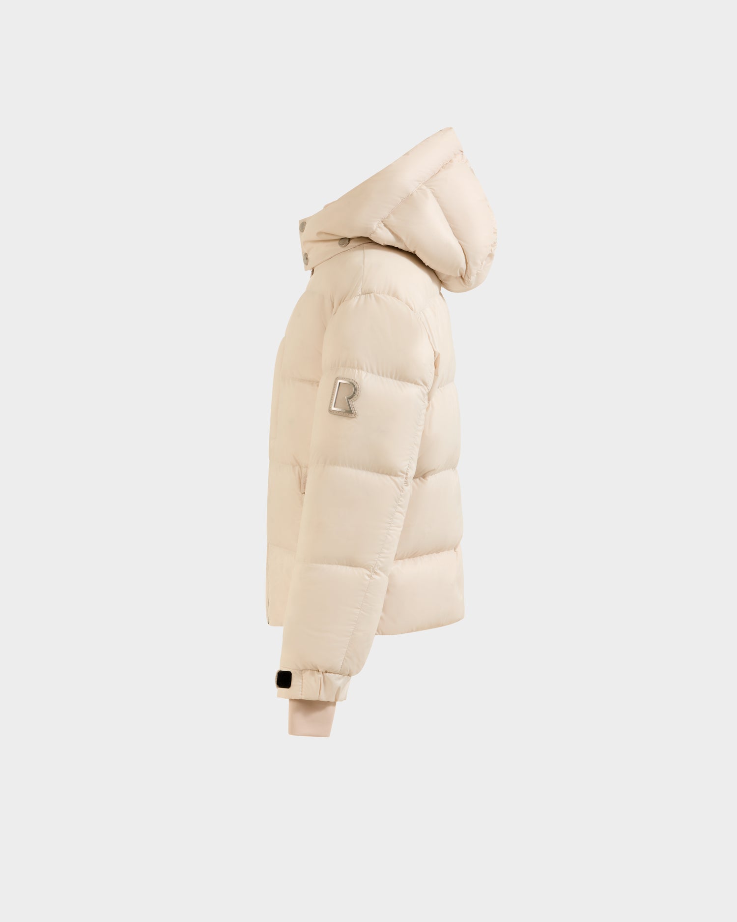 The Rudsak VINCE KS - 0124502 Vanilla is a beige unisex puffer jacket with a hood, RDS-certified down, ribbed cuffs, and an upper sleeve patch with the letter R. Shown from the side against a plain white background.