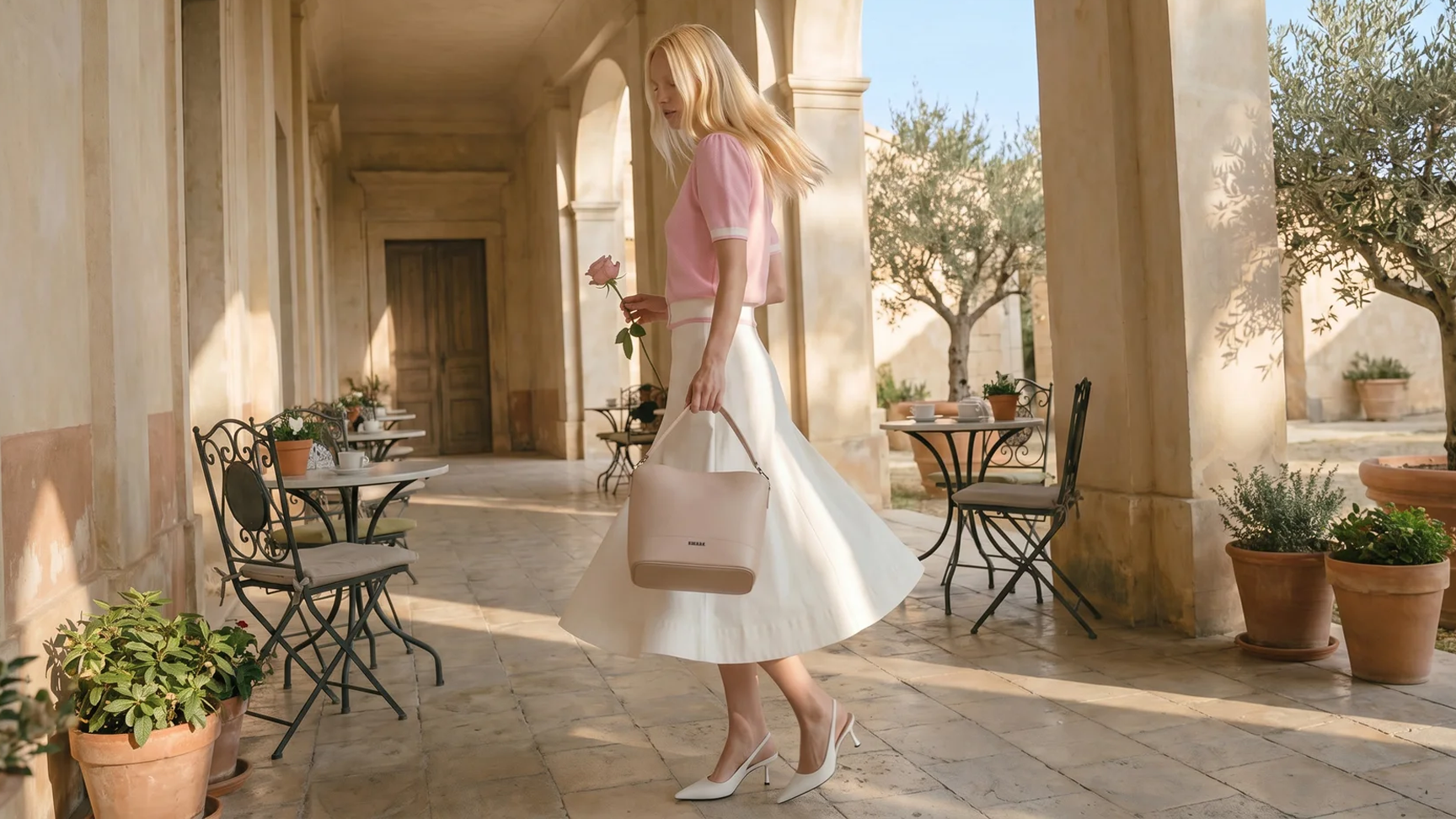 Woman in a white dress holding a beige handbag in an outdoor setting with columns and tables.